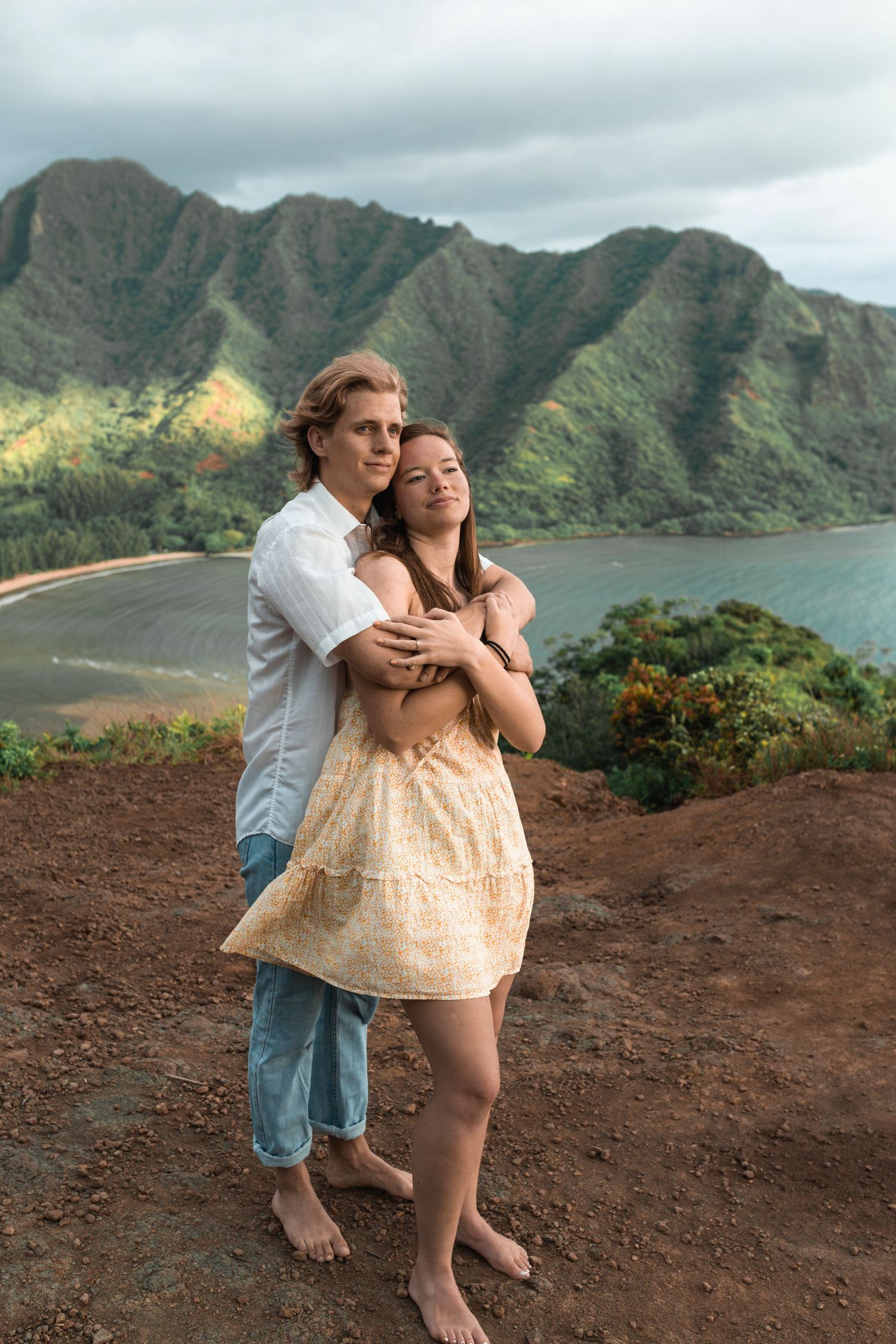 Playful couple sharing intimate moments on volcanic cliff overlooking Hawaiian bay.