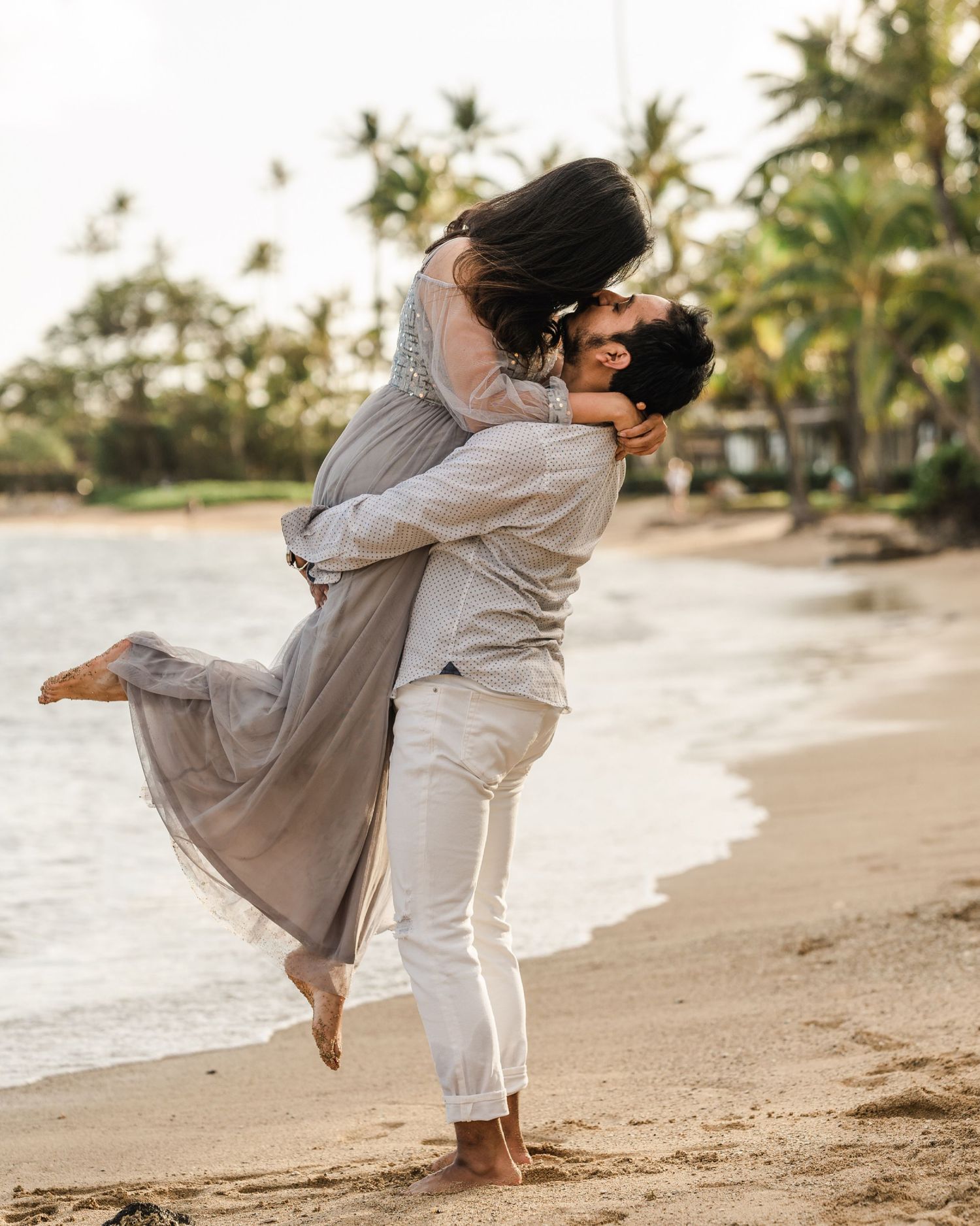 Playful couple dancing and twirling on a tropical beach at sunset with palm trees.