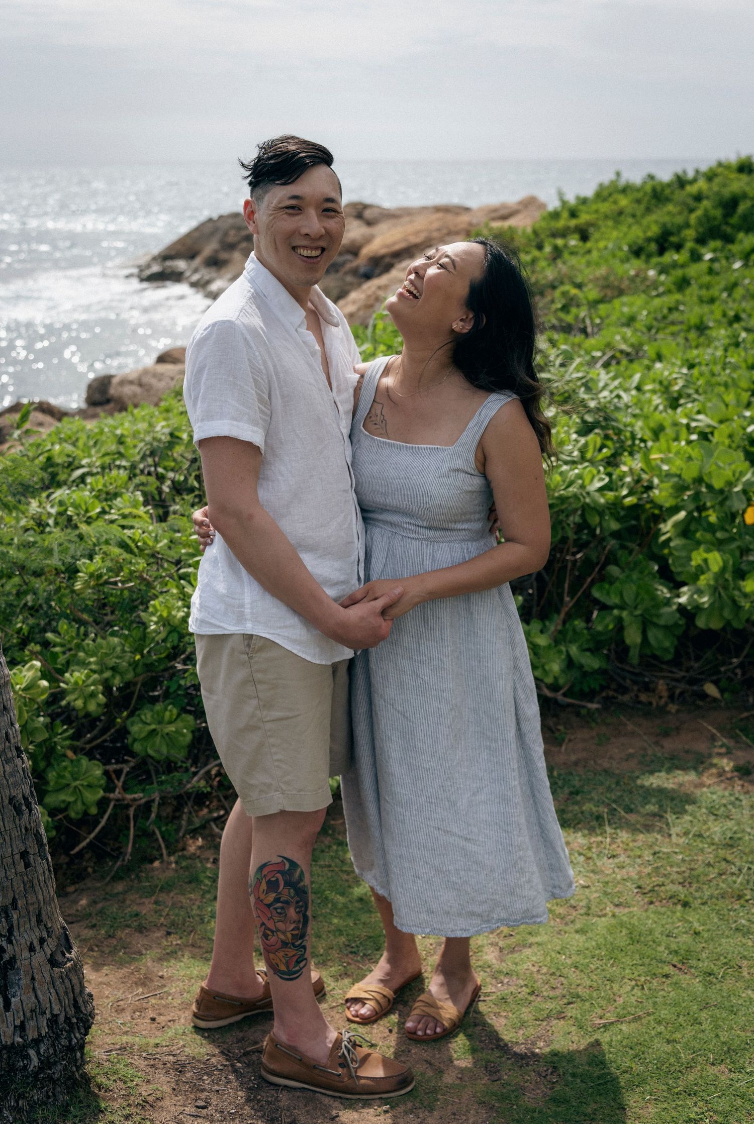 Couple in casual summer attire sharing tender moments on scenic coastal grounds.