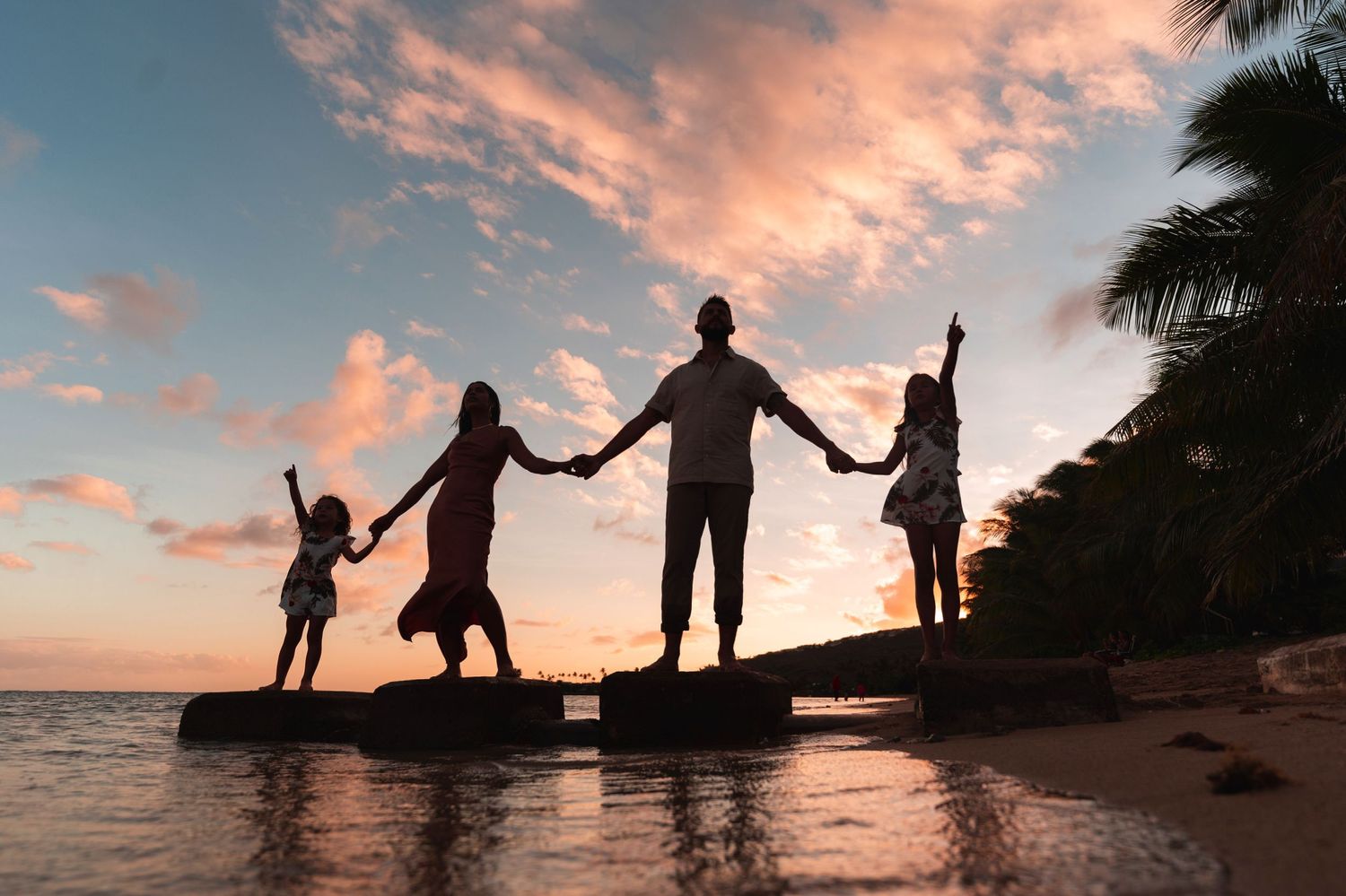 Silhouettes of people against a vibrant sunset sky on a tropical beach.