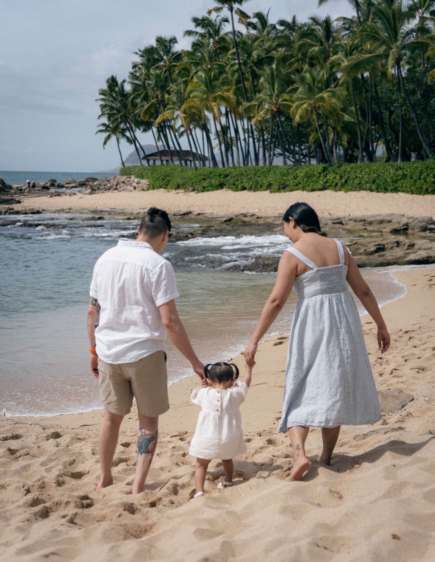 A couple walking together on a tropical beach with palm trees and ocean waves in the background.