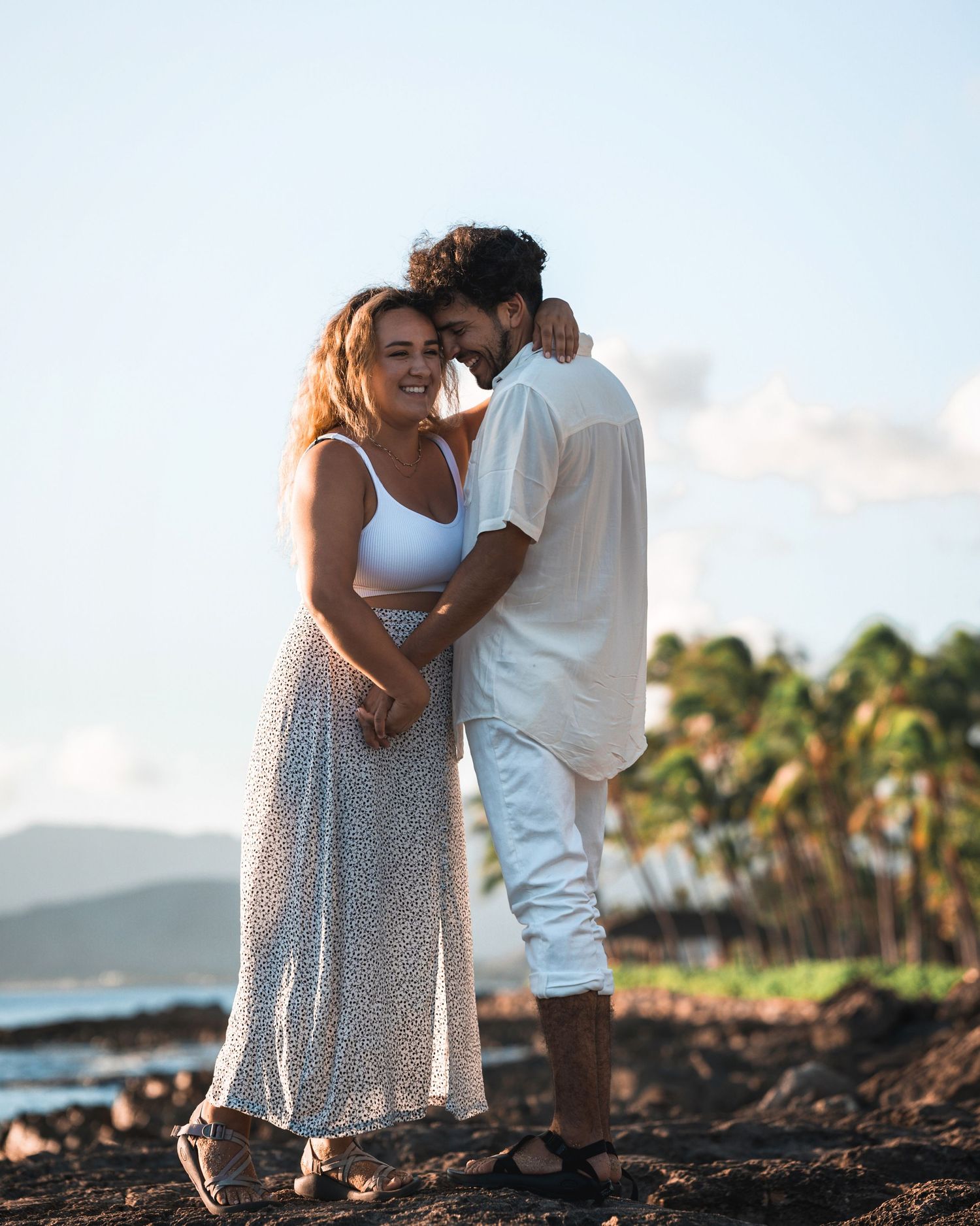 Romantic beach photoshoot with couple embracing against palm tree backdrop at sunset in Oahu.