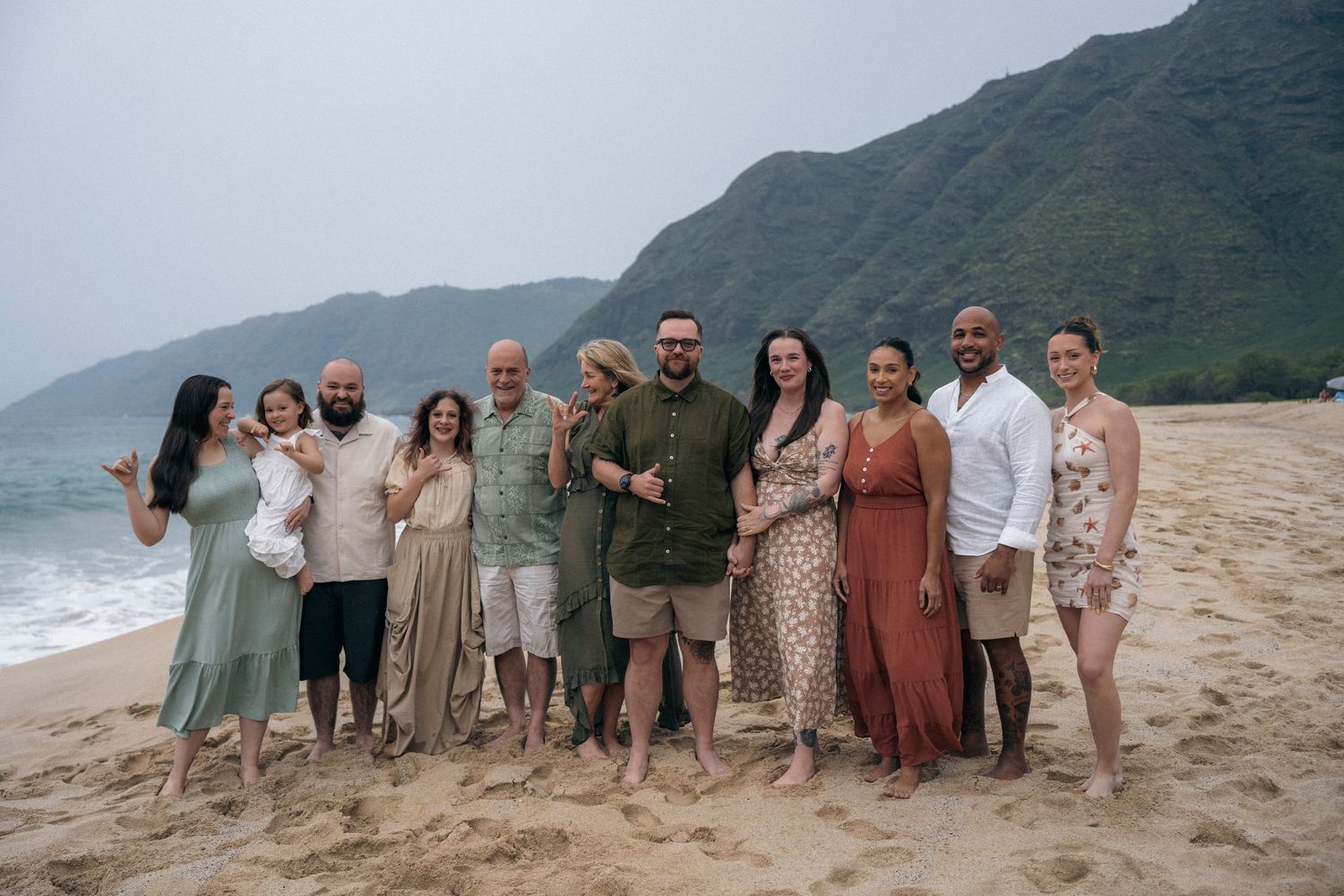 Group portrait of friends and family on a scenic Hawaiian beach with mountains in background.