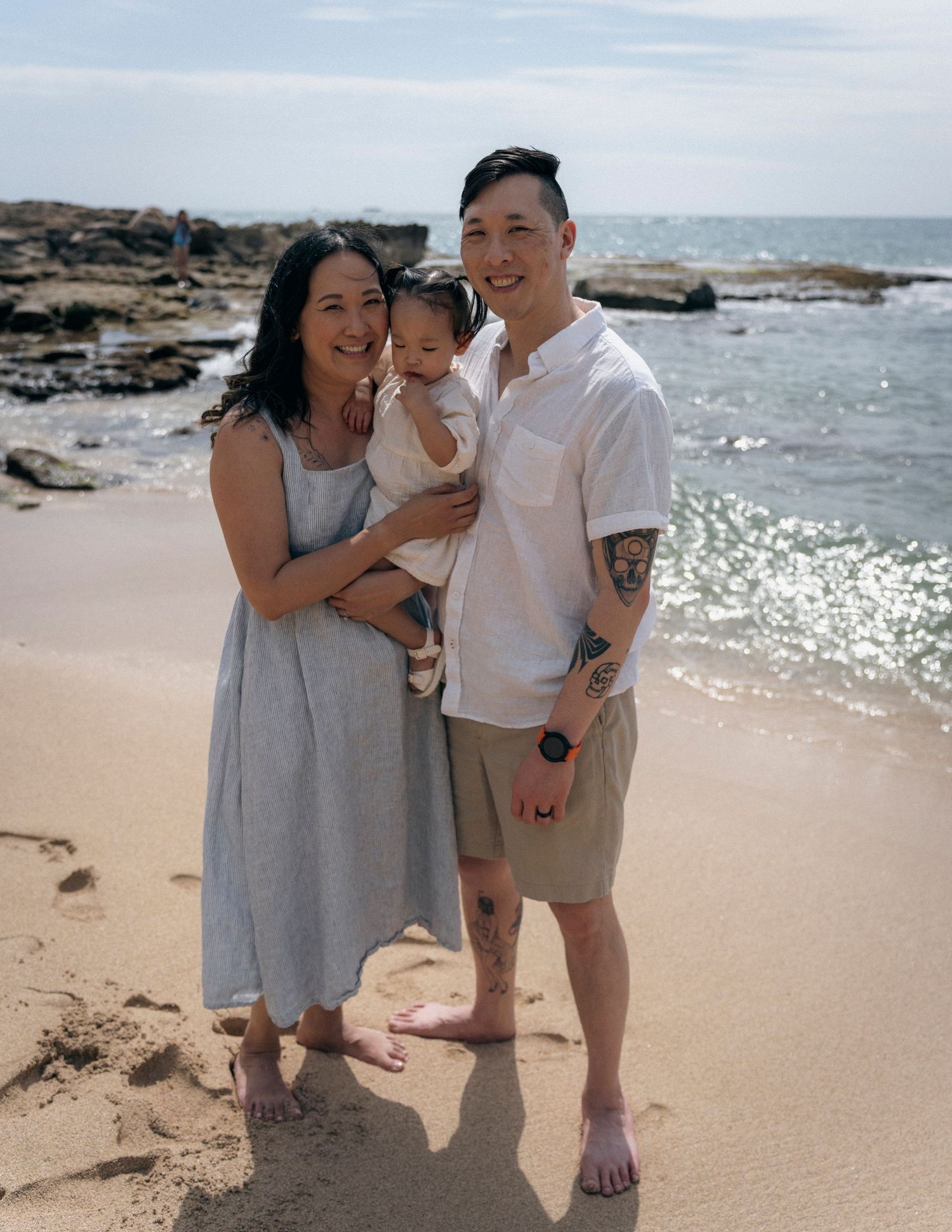 A family poses together on a rocky beach with sparkling ocean waves in the background.