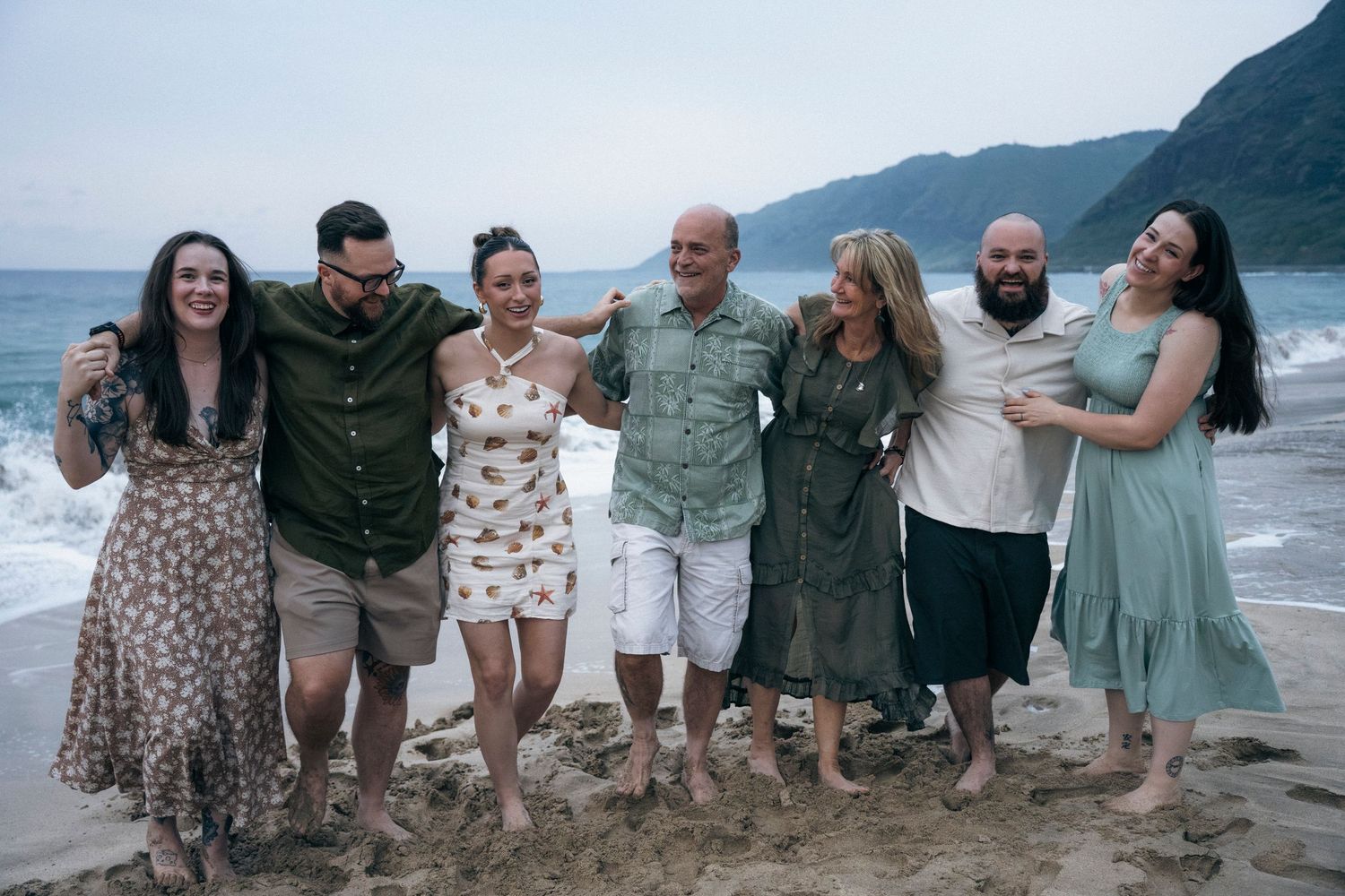 Large group photo on a tropical beach with mountains and ocean waves in the background.