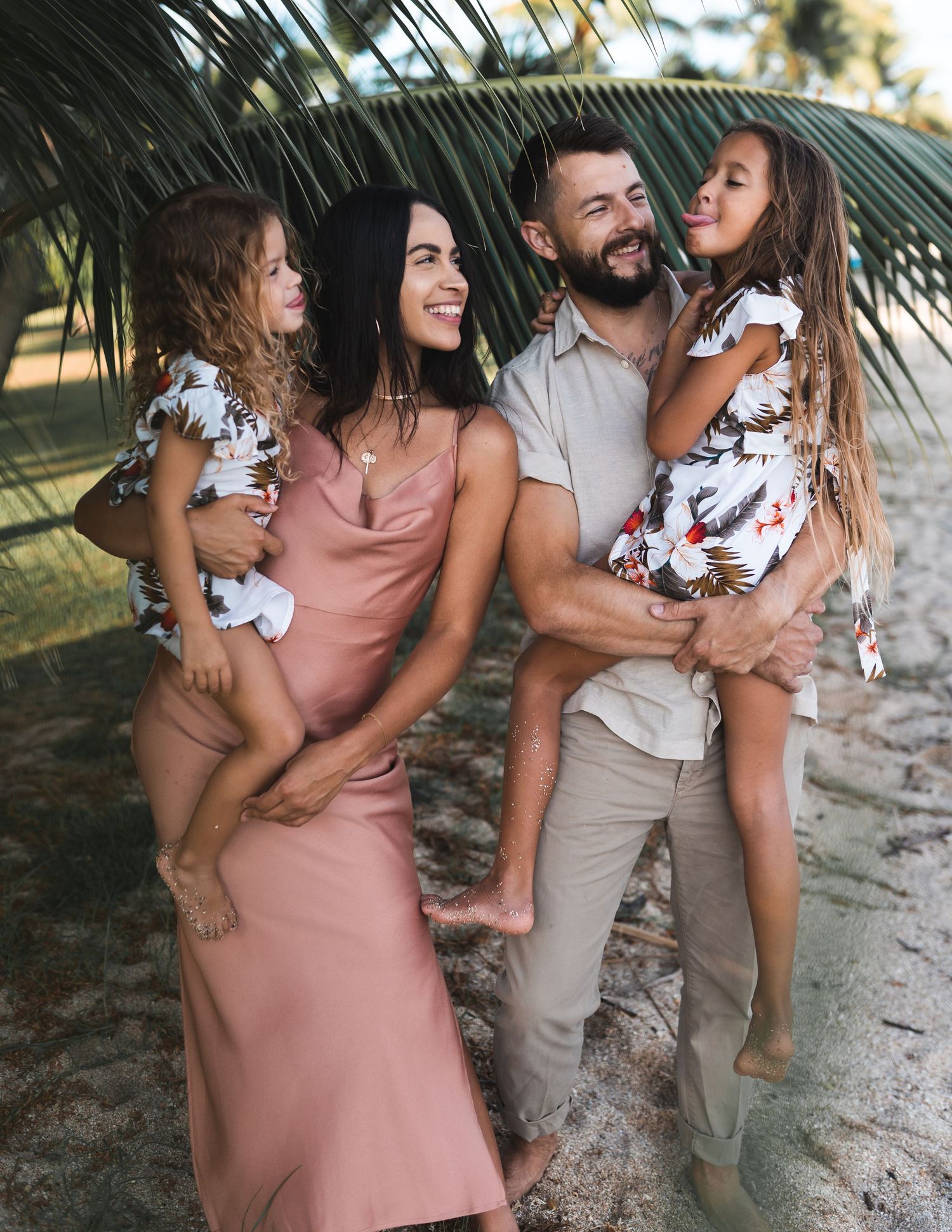 Family enjoying a casual beach day together under palm trees at sunset.