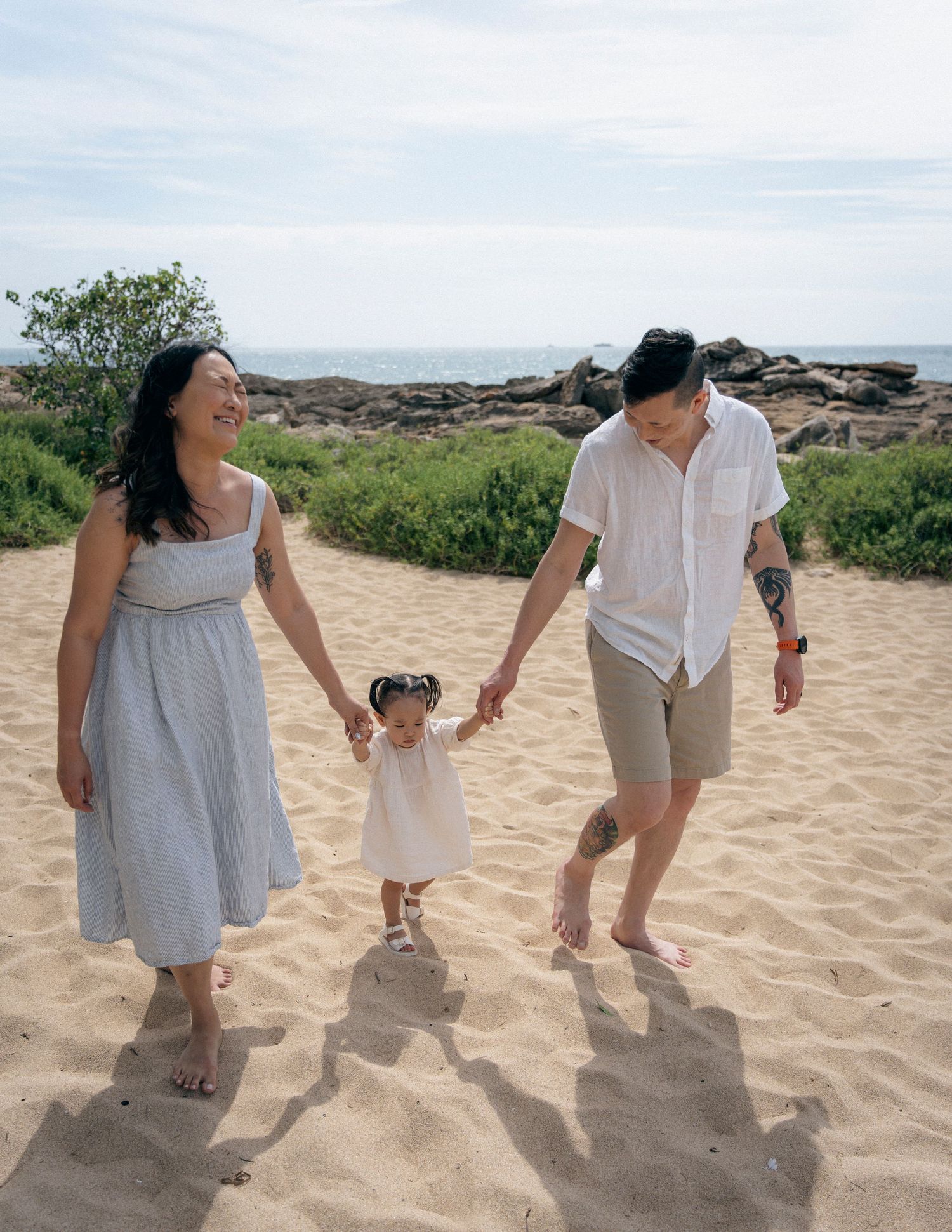 A family holds hands while walking on a sandy beach path near the ocean.