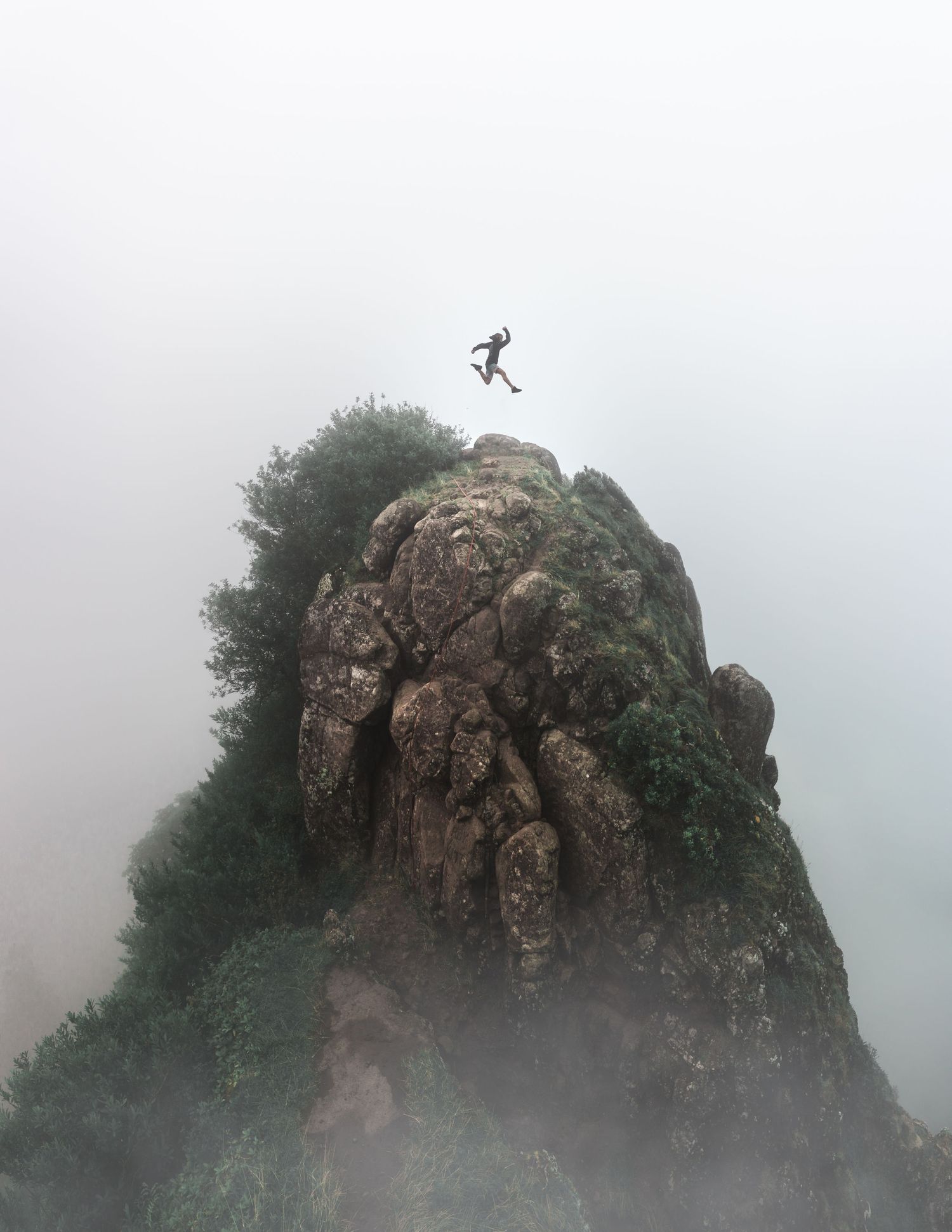 Silhouette of a person jumping between rocky mountain peaks in misty conditions.