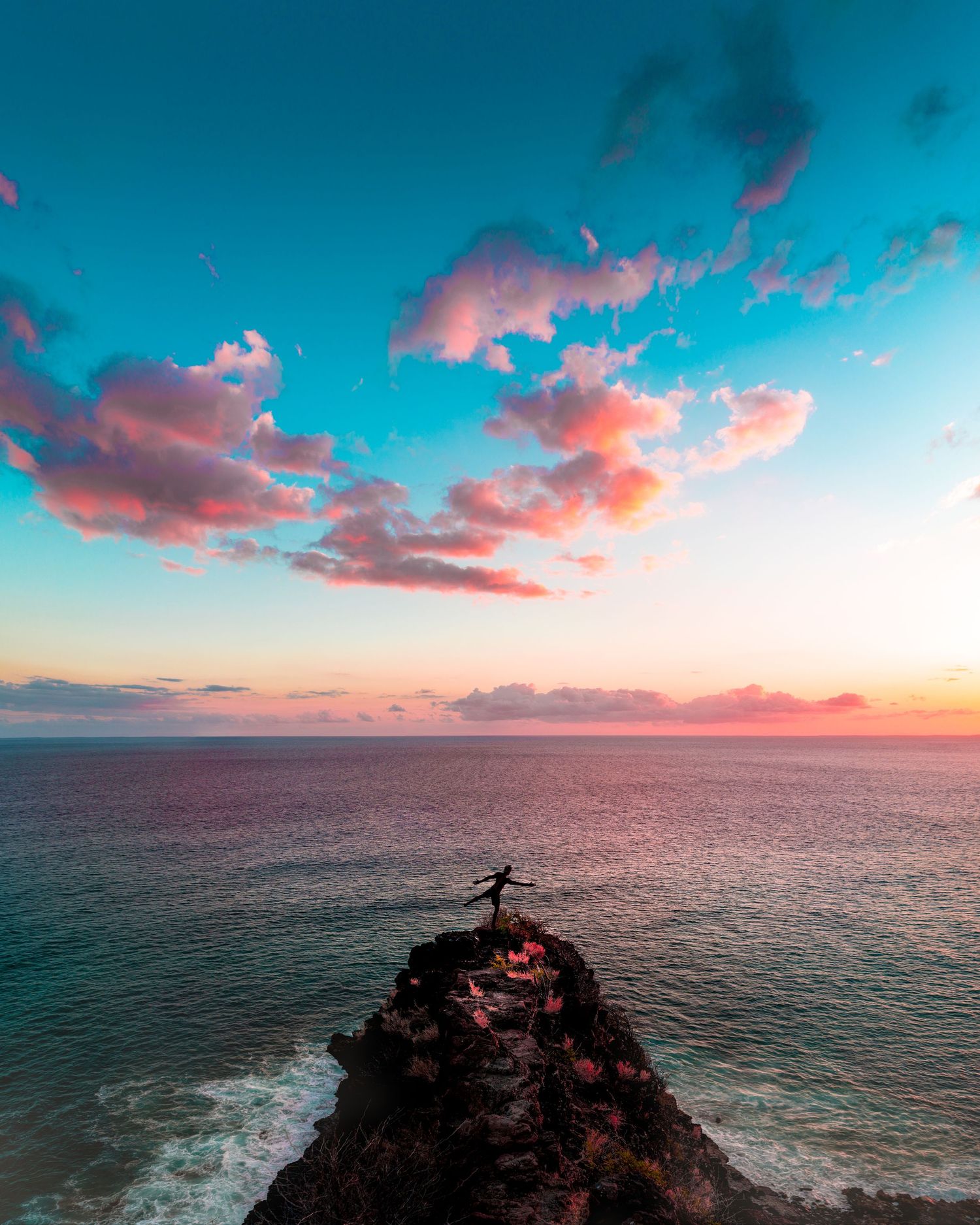 Dramatic coastal cliff landscape with pink sunset clouds over turquoise ocean waters.