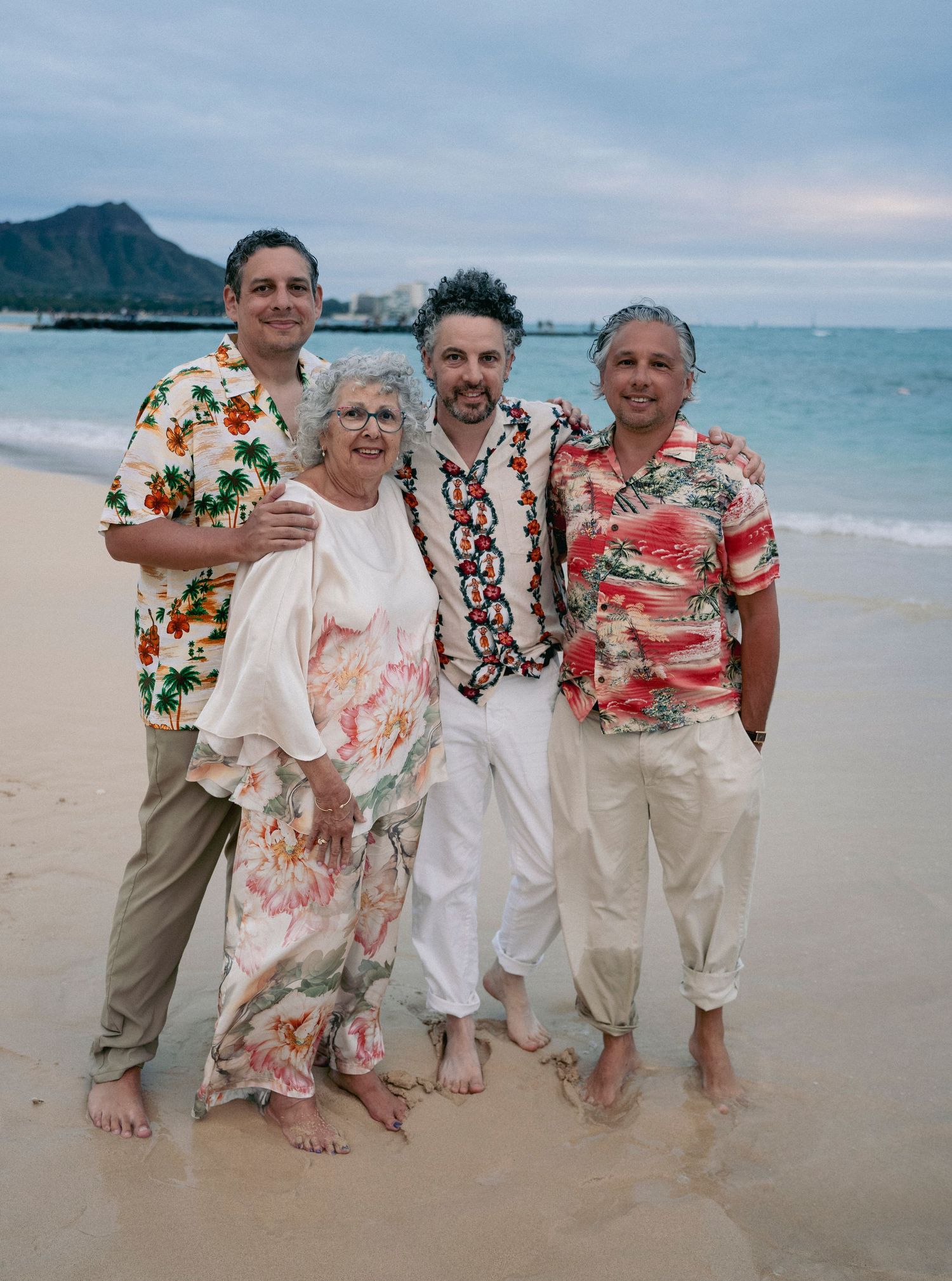 Beach gathering with people wearing coordinated tropical and floral outfits near the ocean.