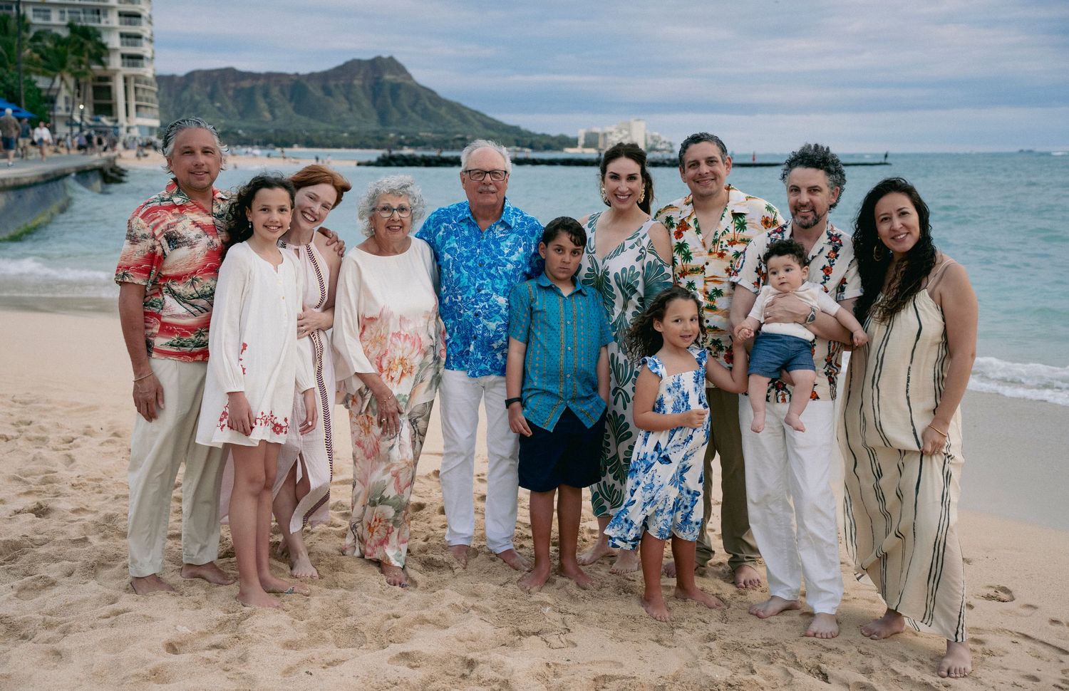 Large family group photo on a beautiful Hawaiian beach with mountain backdrop.