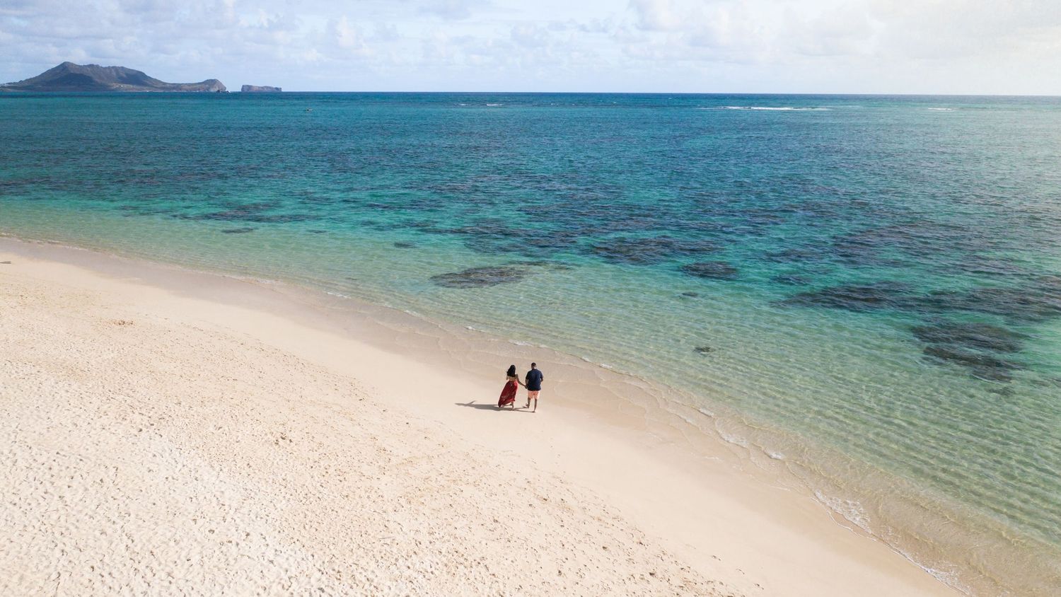 Two tiny figures walking on a pristine white sand beach with crystal clear turquoise waters.