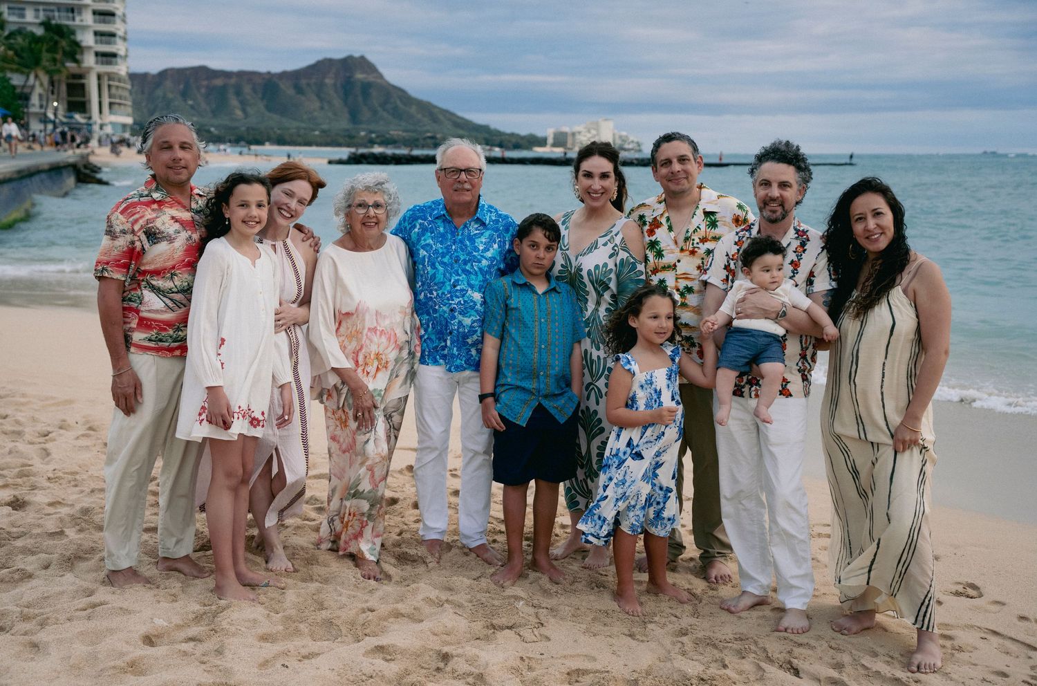 A large family group poses together on a tropical beach with Diamond Head mountain in the background.