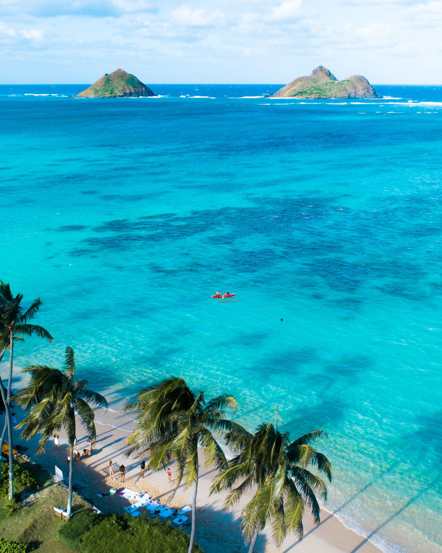 Stunning tropical island landscape in Lanikai with crystal clear turquoise waters, lush palm trees, and distant volcanic peaks.