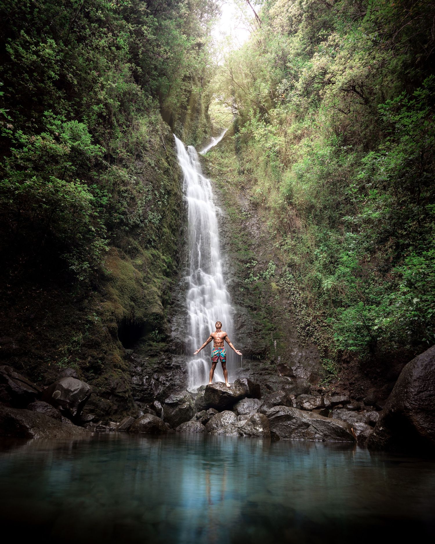 Serene waterfall pool surrounded by tropical vegetation with crystal clear blue water.