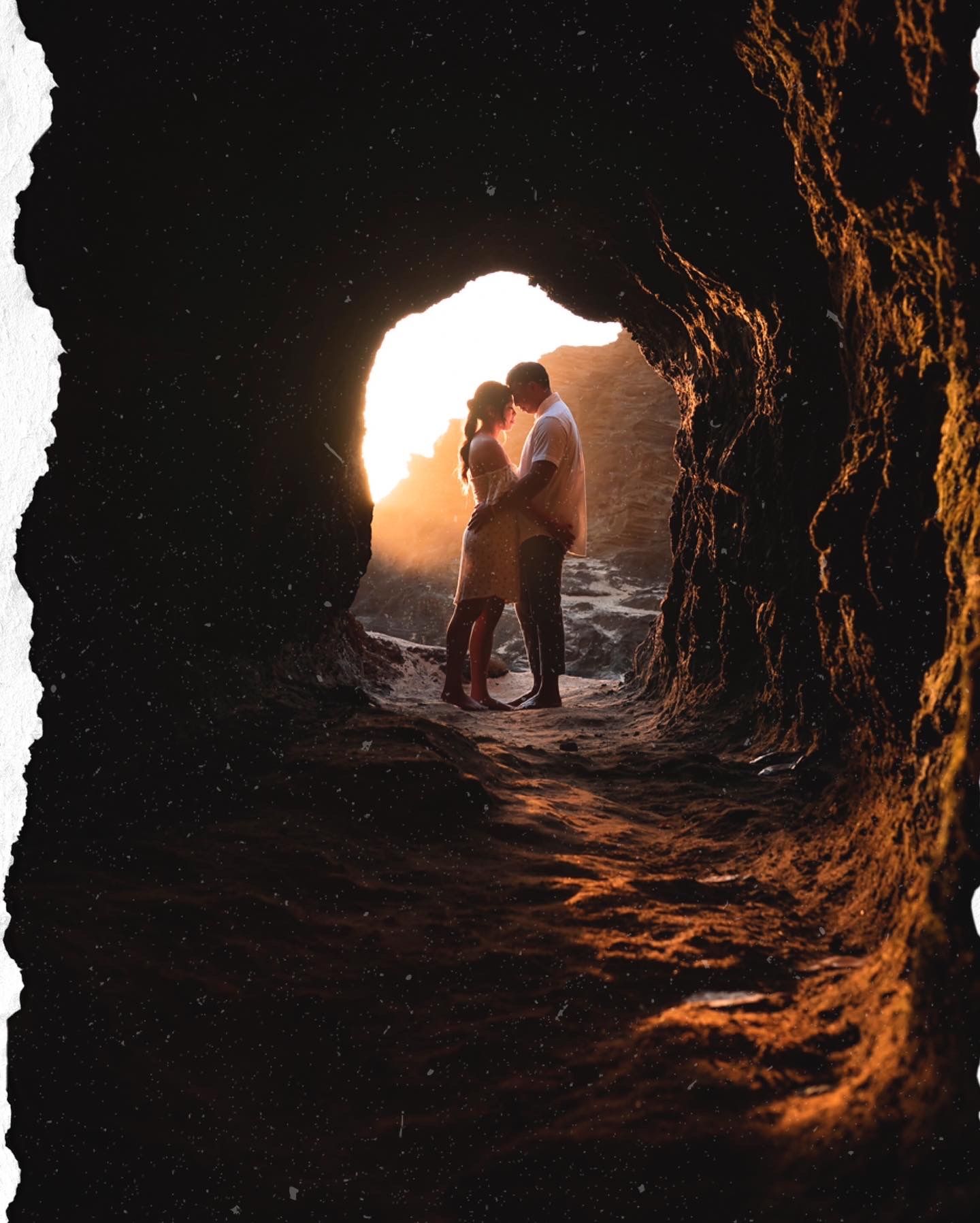 Silhouettes embrace in a sea cave opening with golden sunlight streaming through.