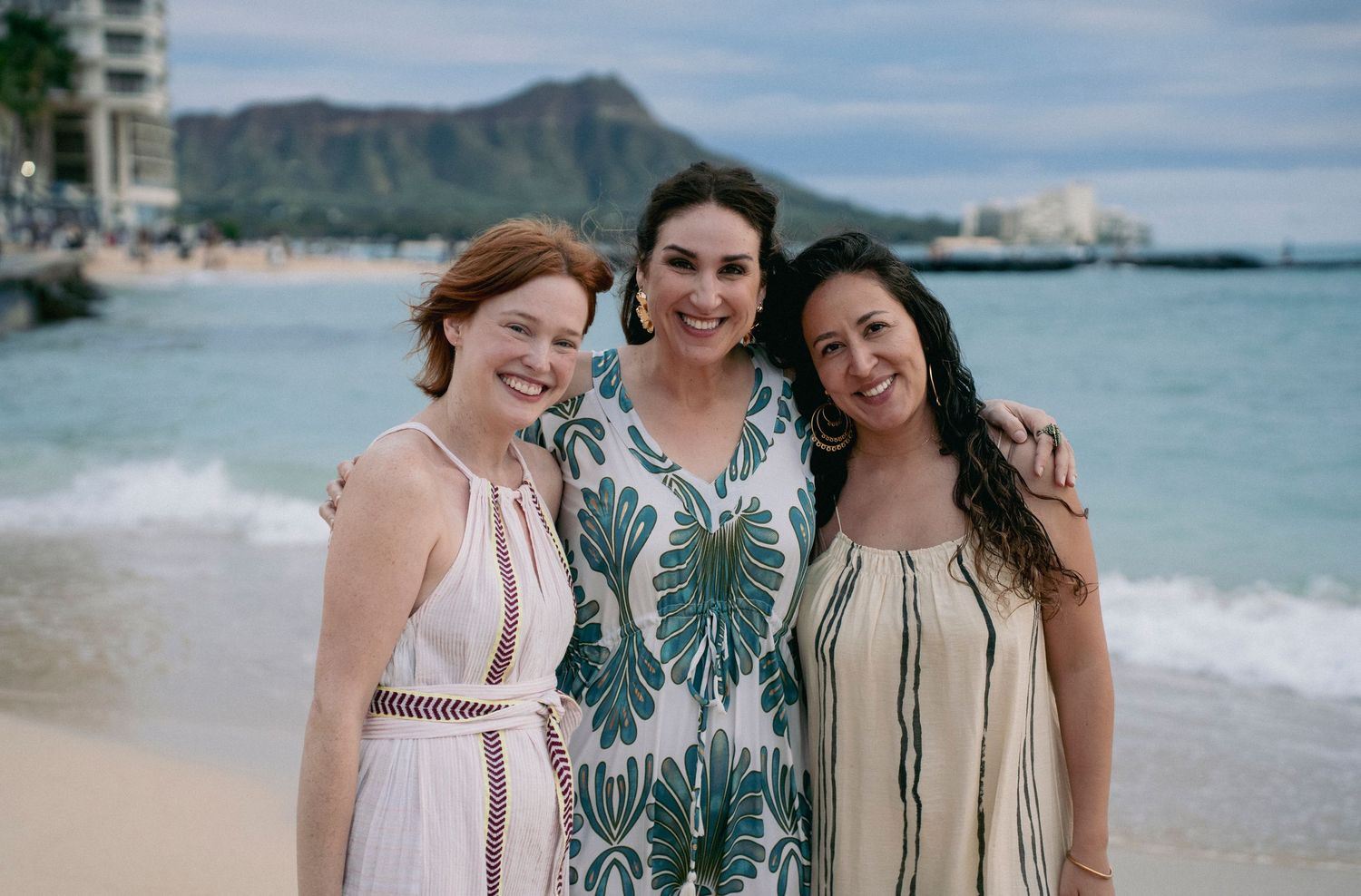 Three friends pose together on Waikiki Beach with Diamond Head mountain visible in the background.