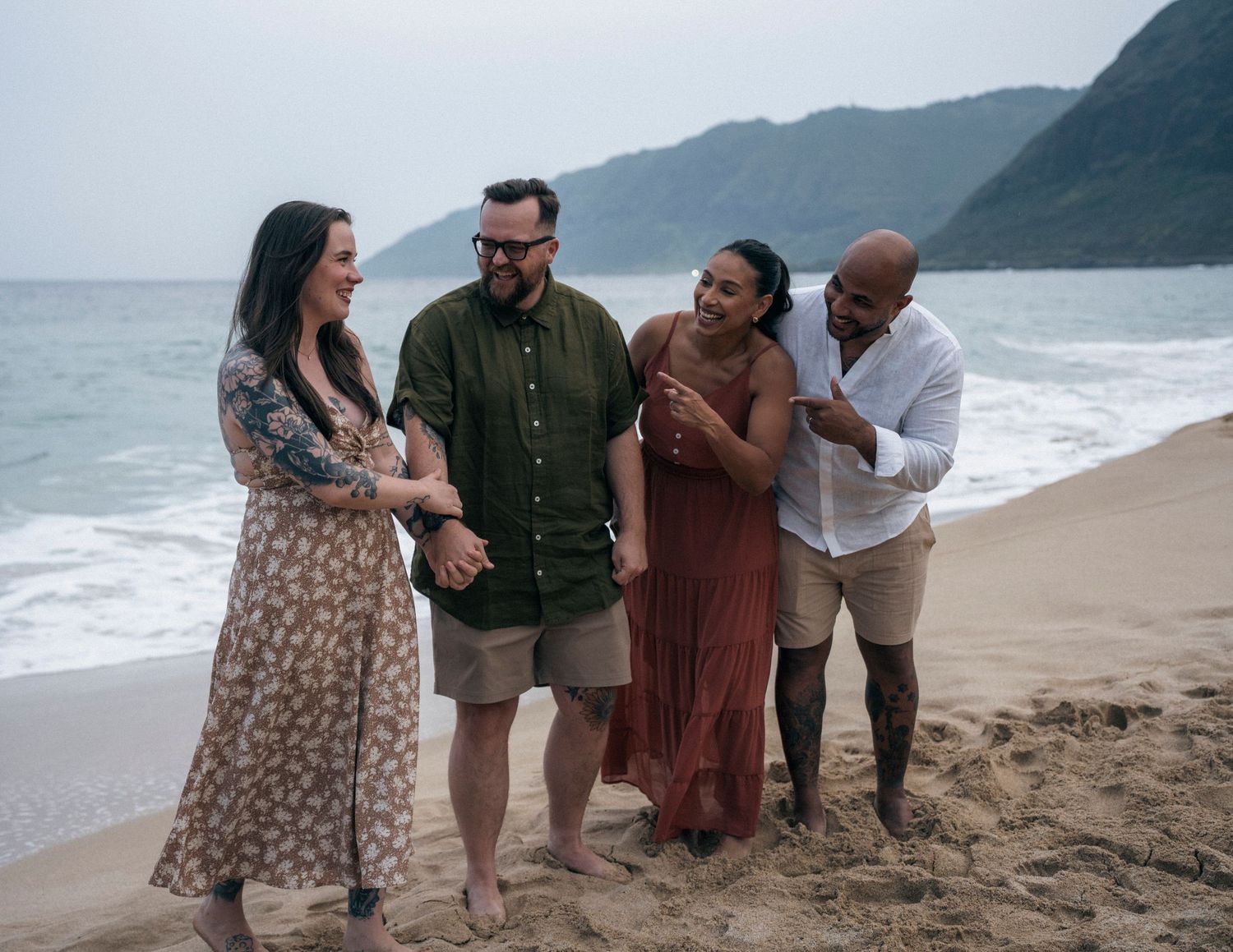 Group gathering on a scenic Hawaiian beach with mountains and ocean waves.