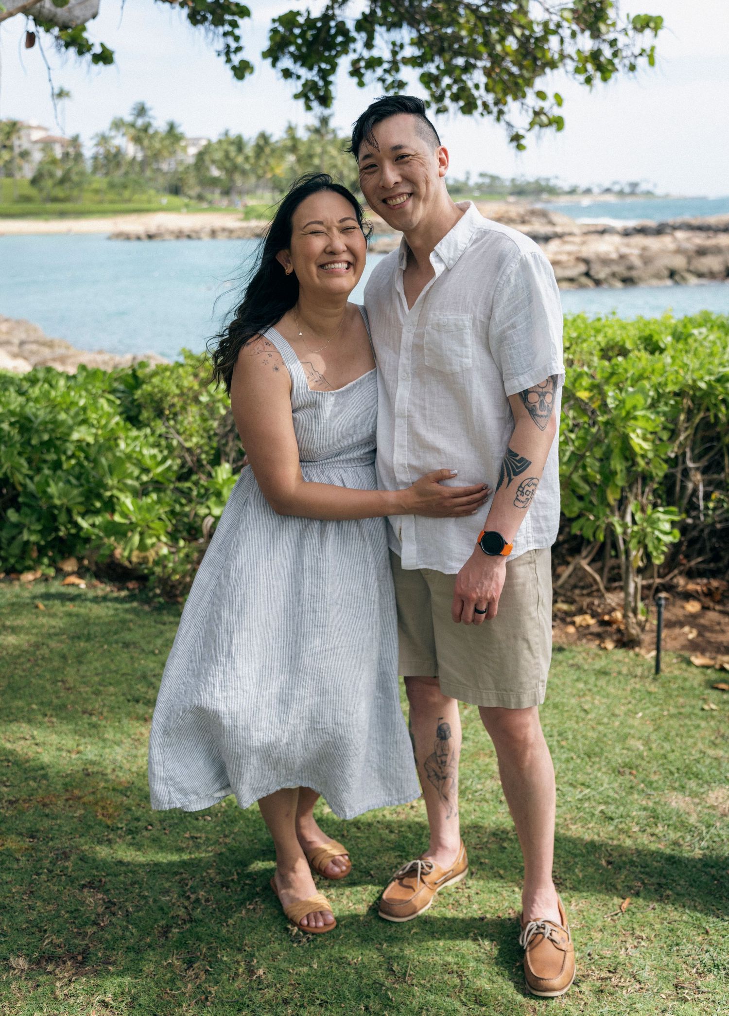 Playful couple in coordinated white and gray outfits posing on grassy oceanfront lawn.
