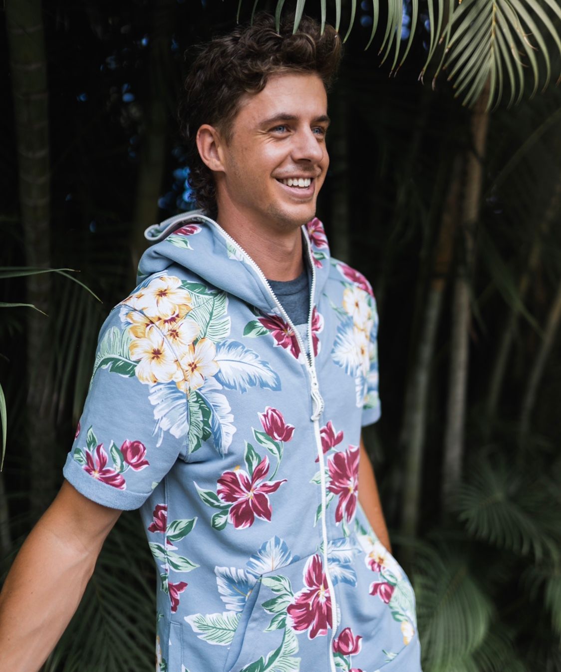 Person wearing a floral print hoodie smiling against a tropical palm background.