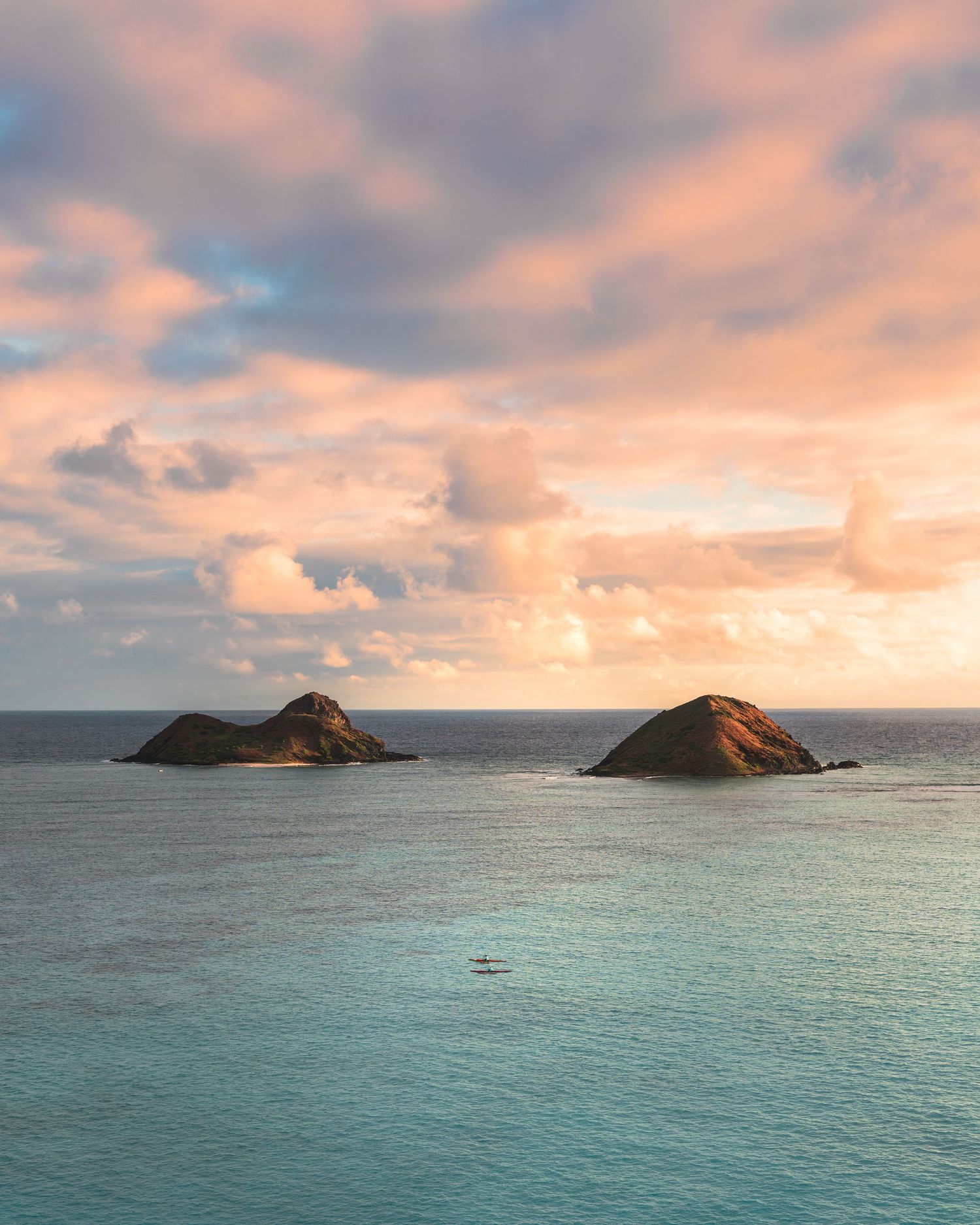 Scenic view of two small islands In Oahu, Hawaii surrounded by turquoise waters and a colorful sunrise sky.