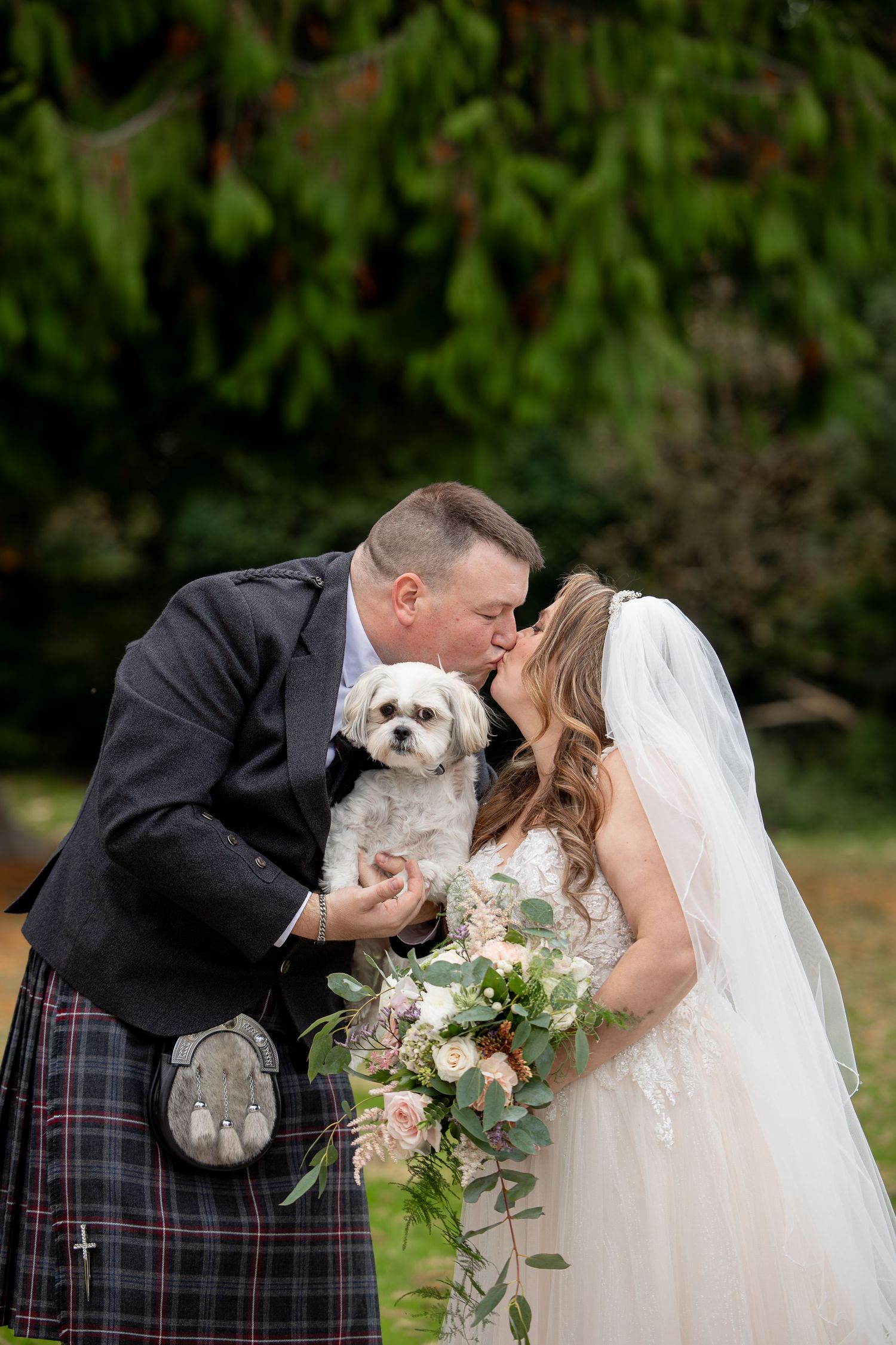 A wedding couple shares romantic kisses in a series of photos while holding their small white dog and floral bouquet.