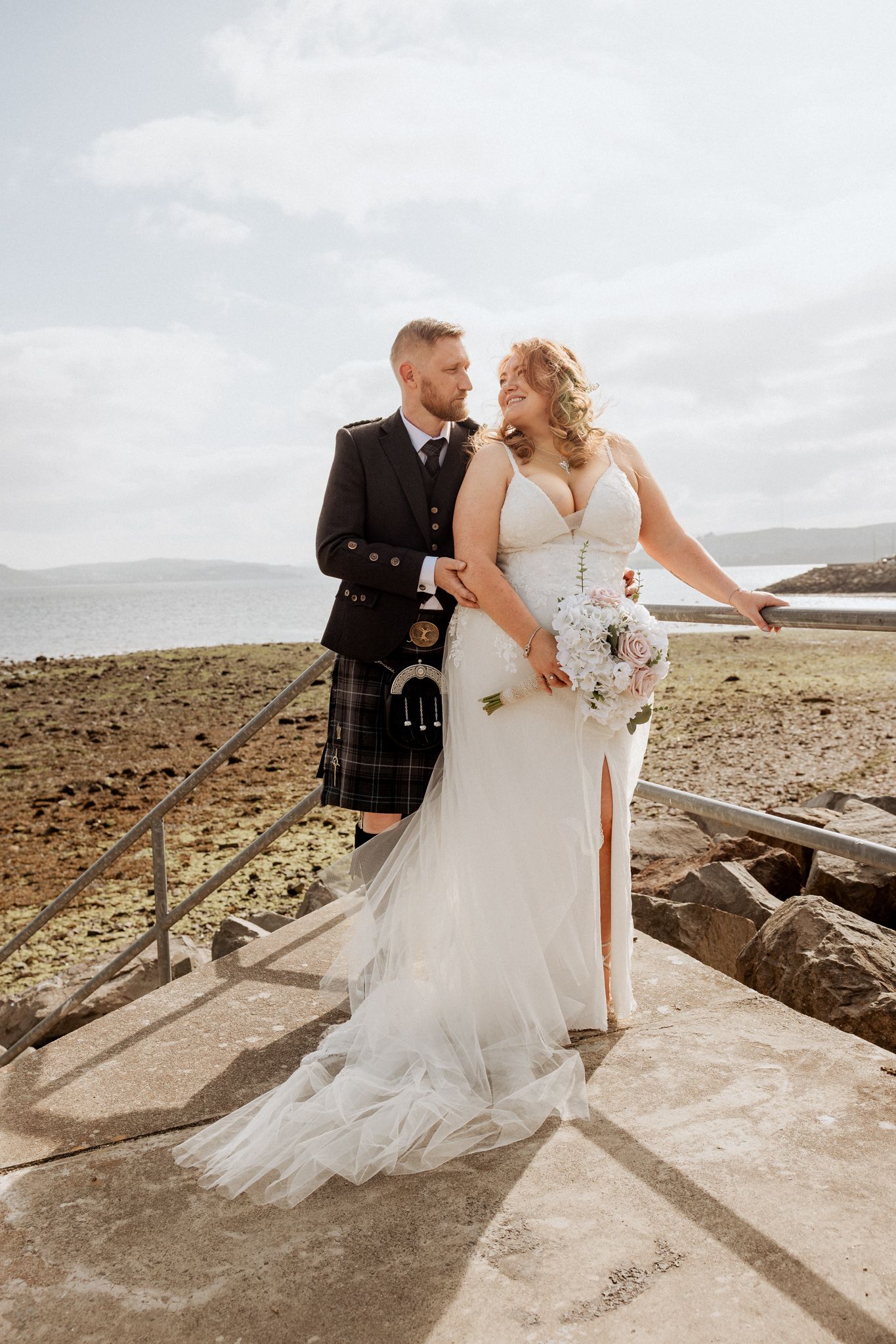 A Scottish wedding couple poses on coastal cliffs with dramatic cloudy skies in the background. Helensburgh Civic Centre