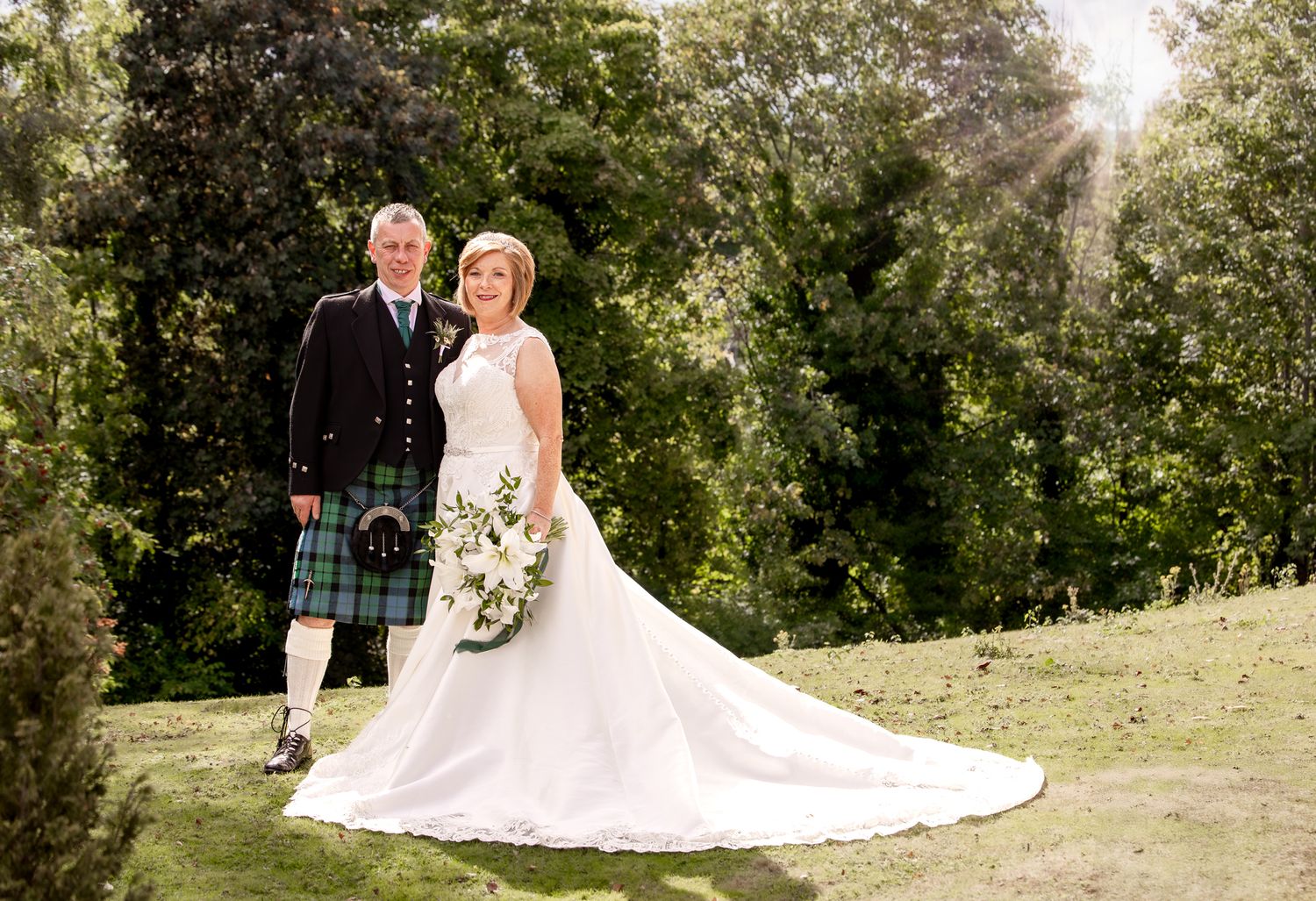 Wedding couple poses in multiple romantic outdoor settings with sunlit trees and natural greenery in the background.