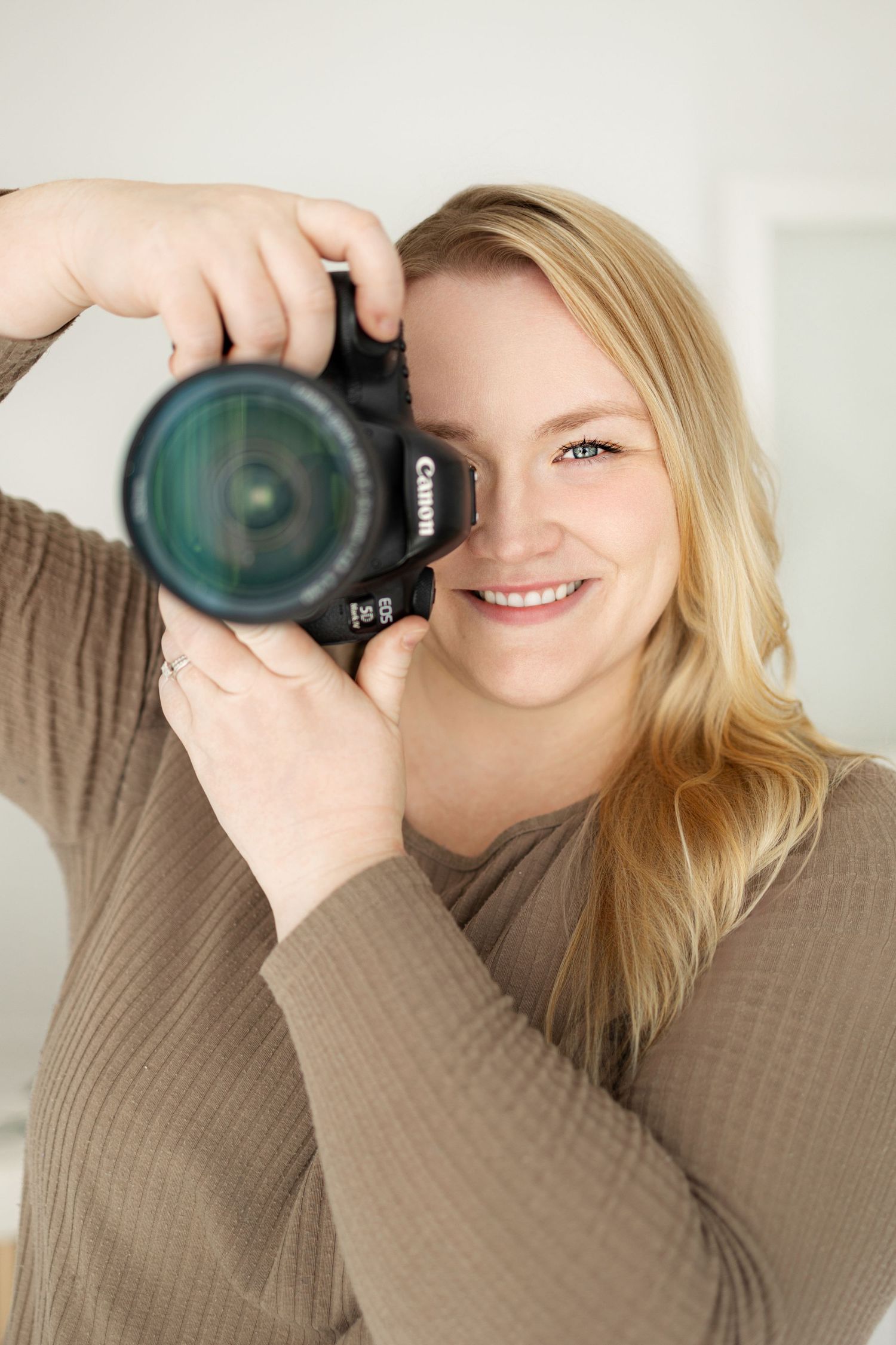 Photographer holding camera lens in cozy beige sweater against light background.