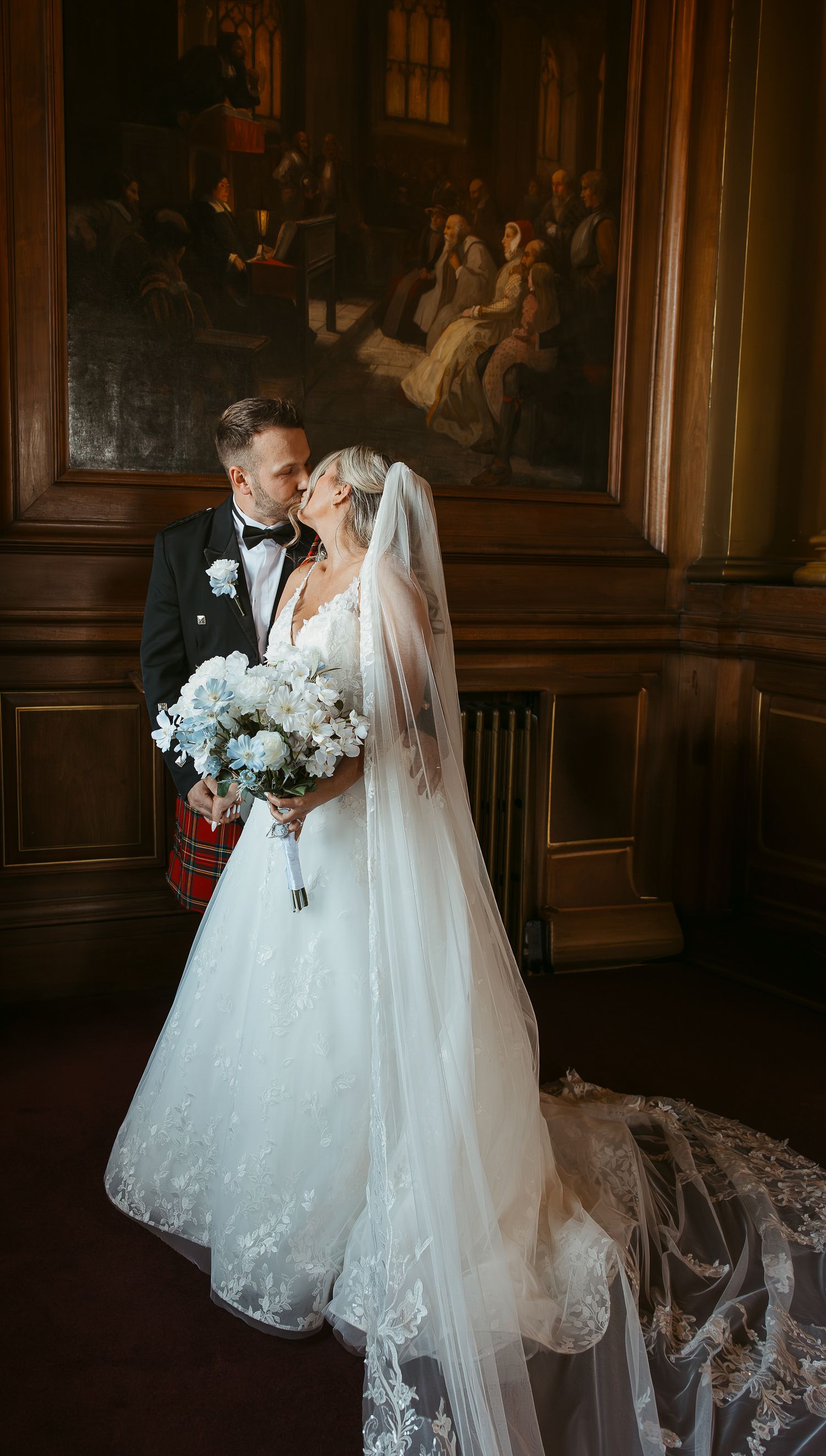 Romantic wedding couple sharing intimate moments in an elegant wood-paneled room with dramatic lighting and flowing veil.