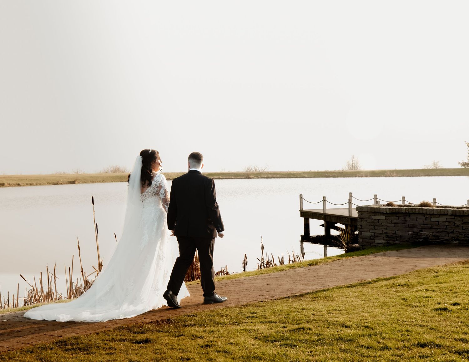 A couple walks along a scenic waterfront path during sunset with white fabric flowing in the wind.