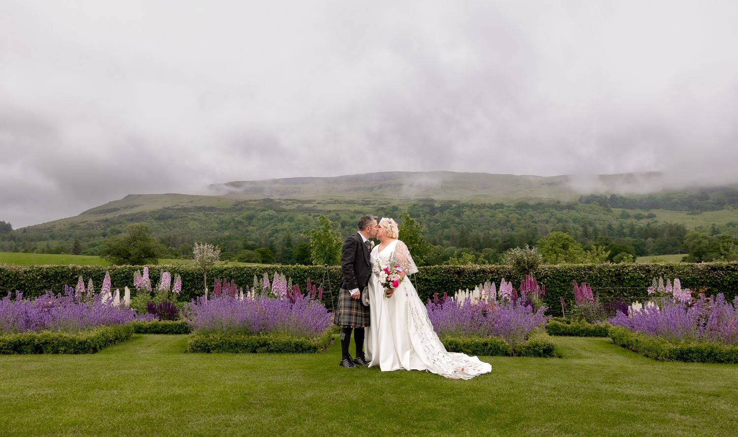 Wedding couple poses in scenic mountain landscape with purple wildflowers in the background. Fintry