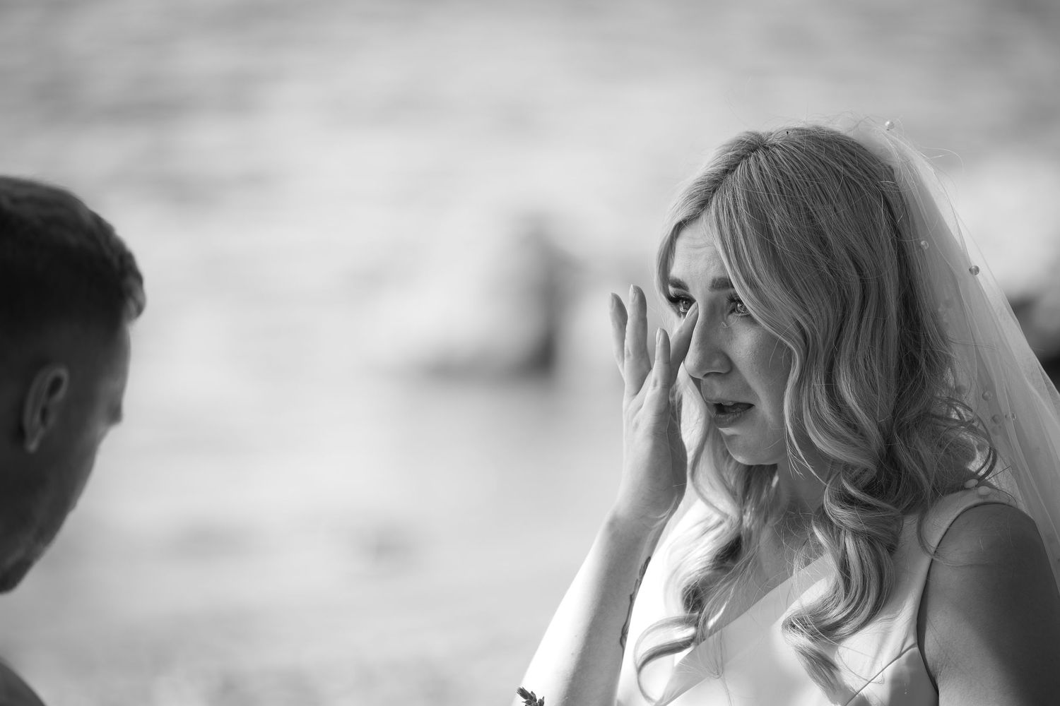 Black and white photo of an emotional bride wiping tears during her outdoor wedding ceremony.