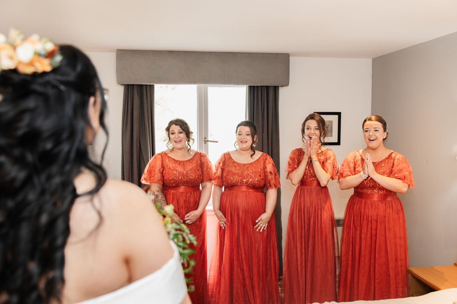 Bridesmaids in vibrant red dresses share joyful moments during wedding preparations.