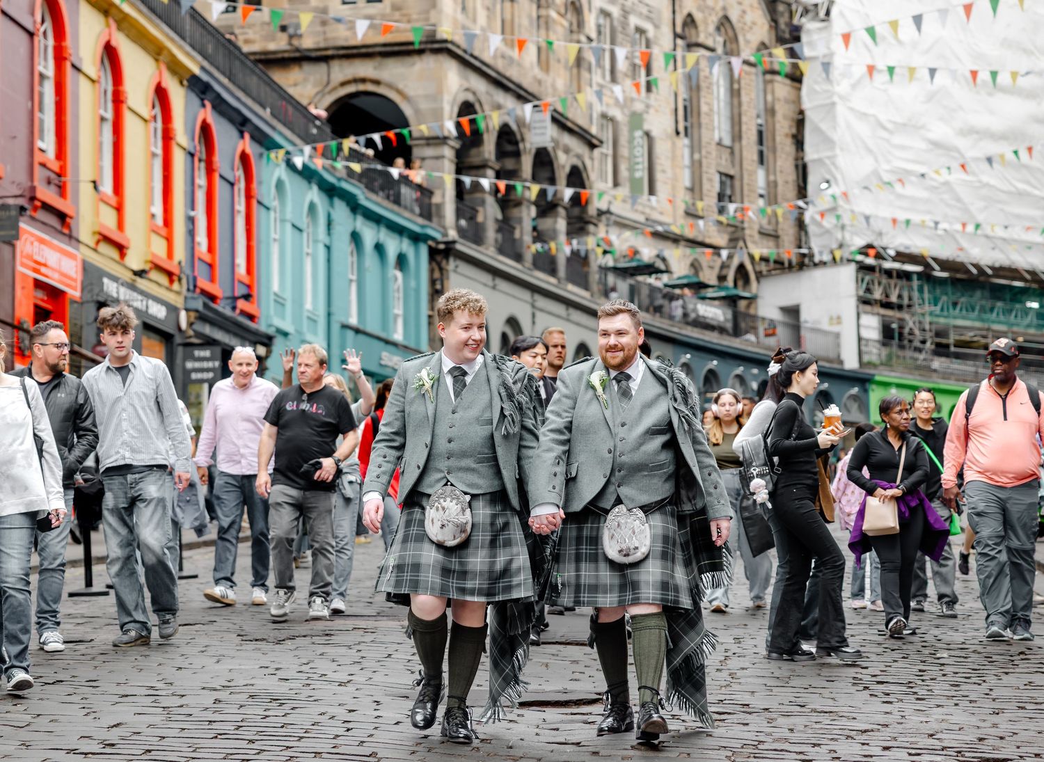 Two men in traditional Scottish kilts walk along a cobblestone street in Edinburgh, Scotland.