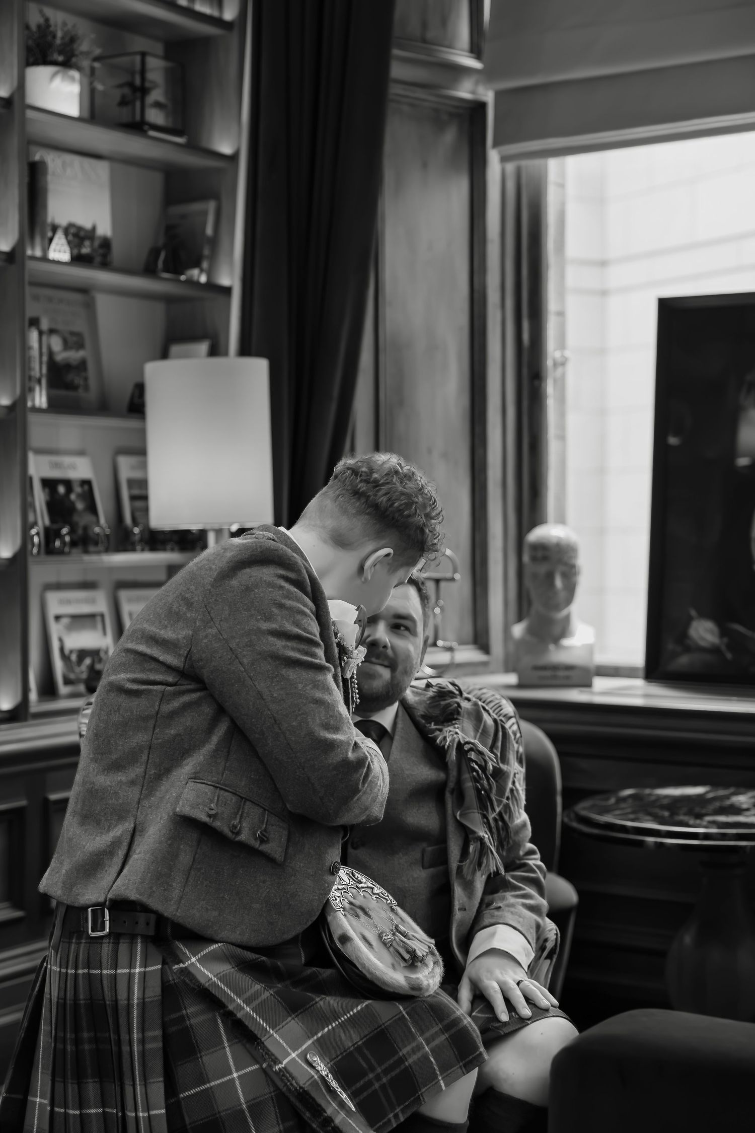Black and white photo of two grooms in kilts sharing an intimate moment in an elegant Scottish wedding venue.