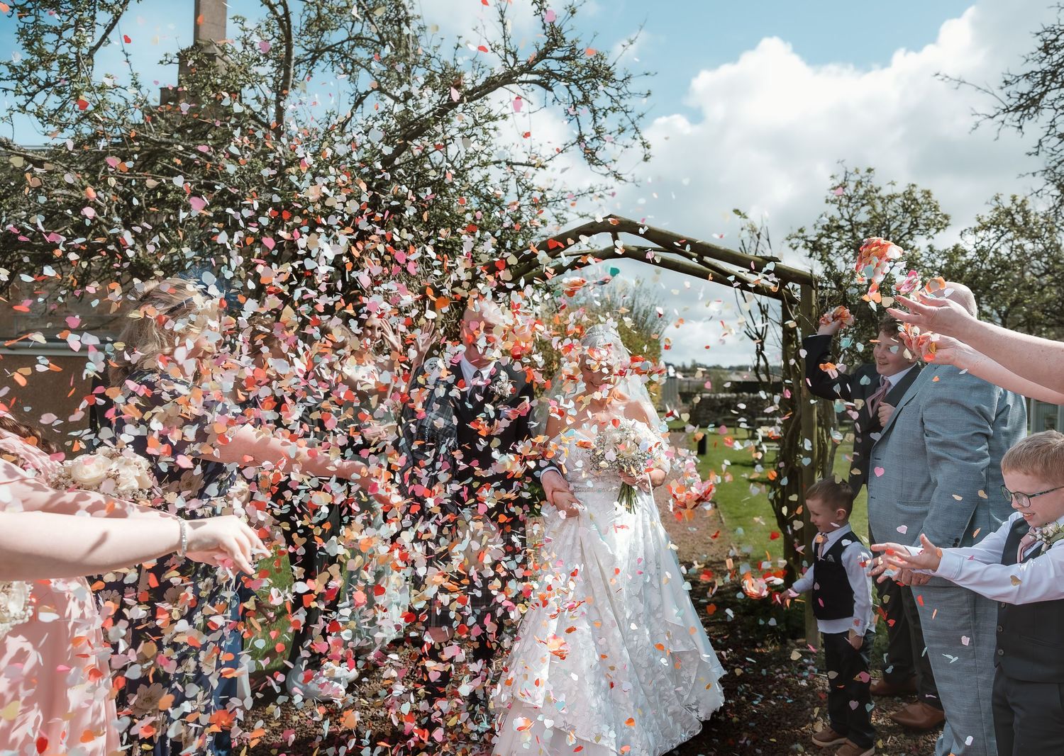 Bride and groom celebrate with colorful confetti shower at outdoor rustic wedding ceremony.