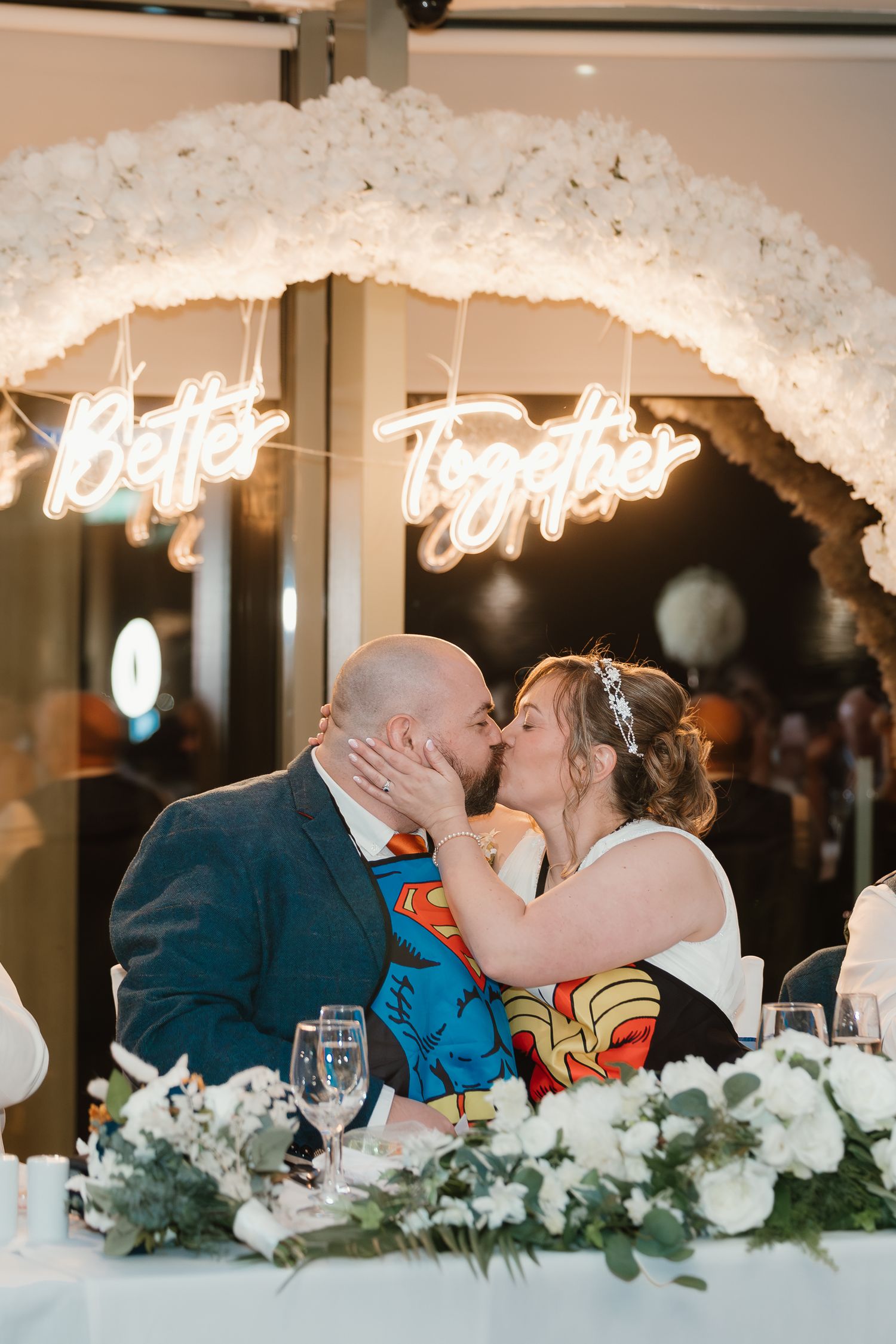 Wedding reception table with floral arrangements under illuminated neon signage.