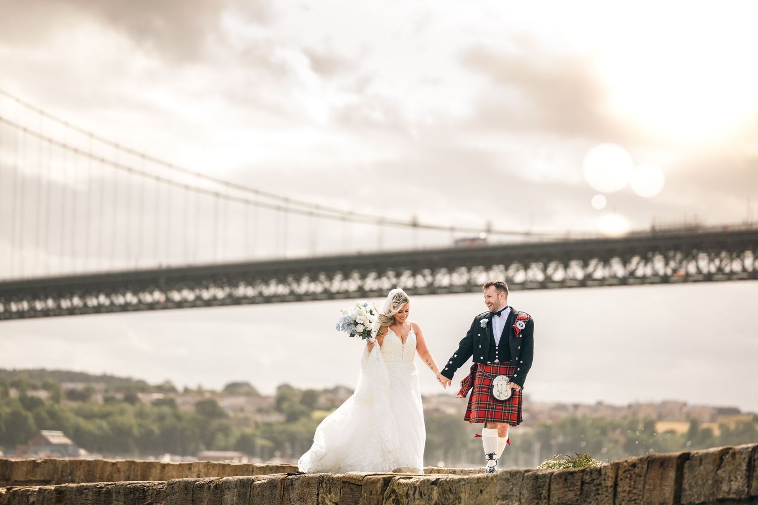 Wedding couple poses beneath a massive suspension bridge on a cloudy day.
Doubletree South Queensferry