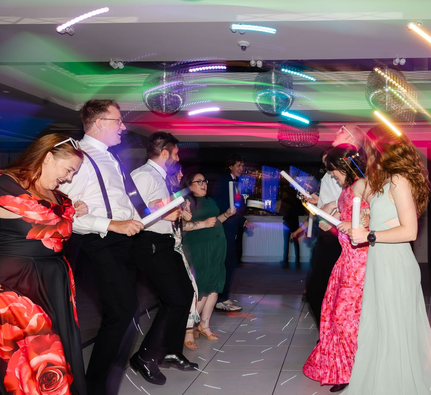 Group of young adults dancing and singing at a colorful neon-lit party or prom event.