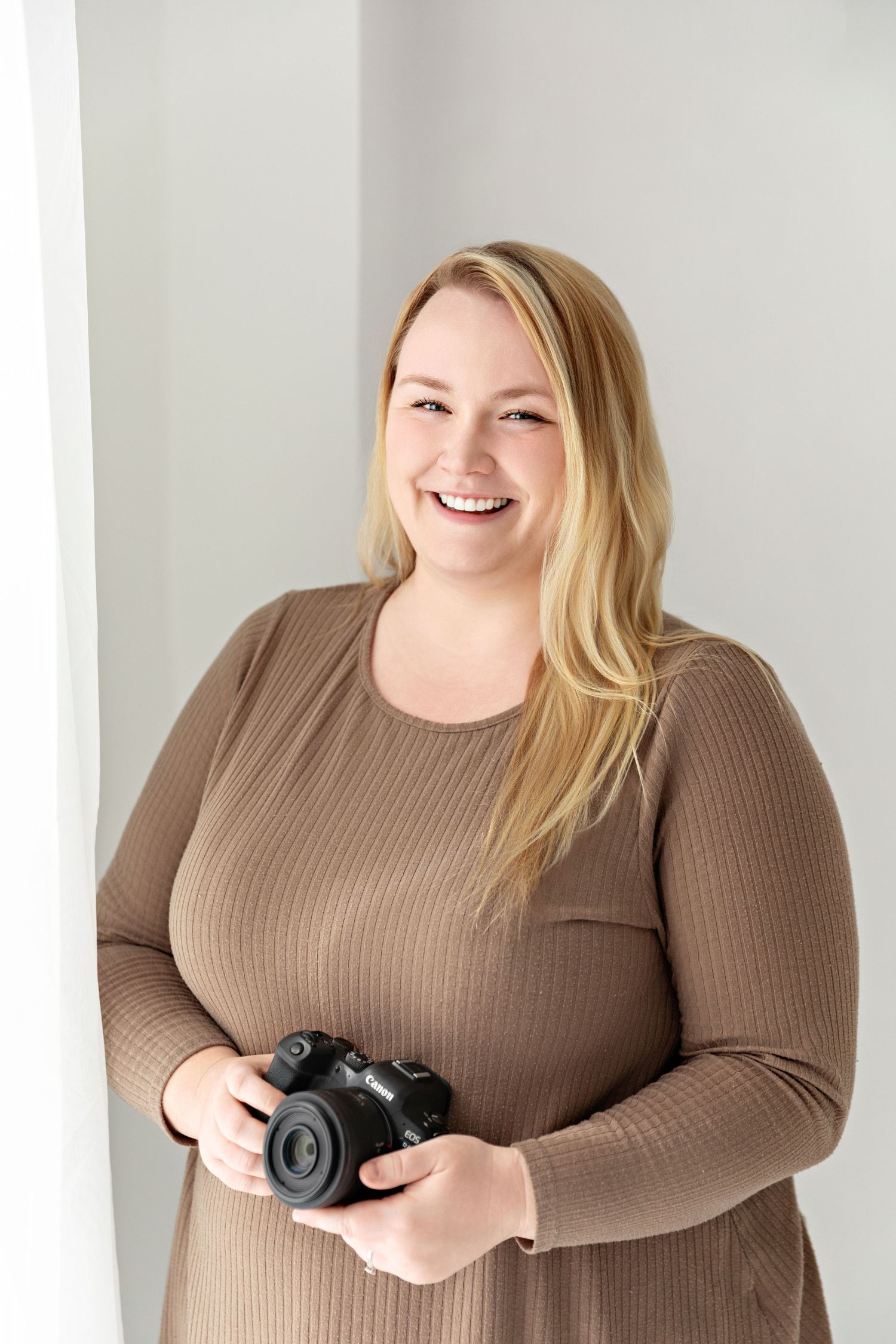 Professional photographer holding a camera against a white studio backdrop.