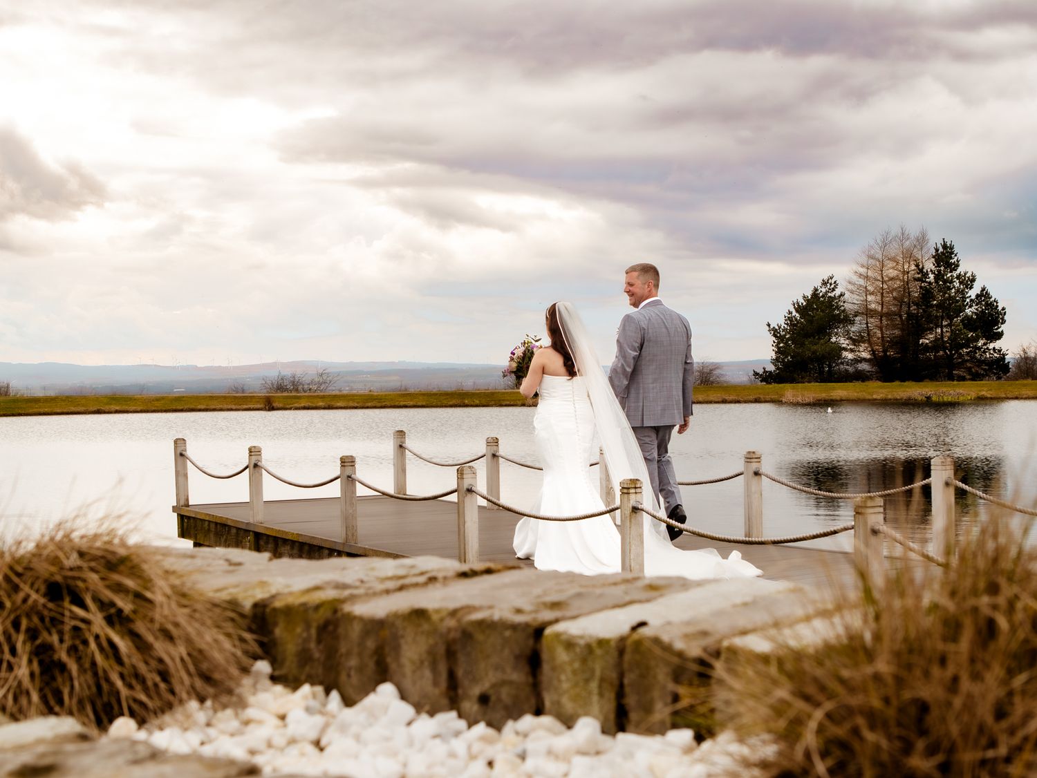 Romantic wedding photos on wooden pier with dramatic cloudy sky and natural landscape. The Vu