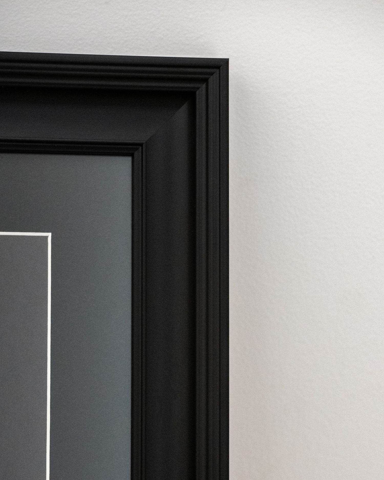 A close up of black signature wall art framing showing detail of frame & mount & anti reflective glazing to create a minimalist pattern.