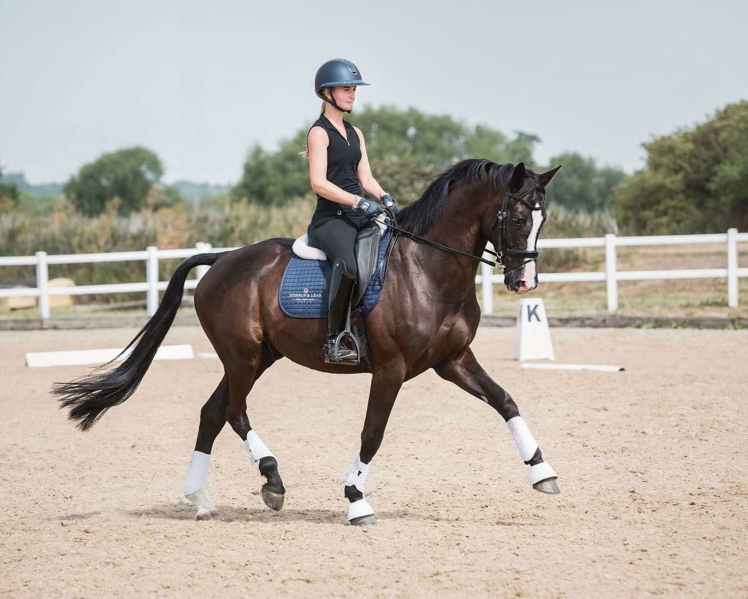 Dressage rider performing movements in sandy arena at Bury Farm dressage on big warmblood with floating extension of the trot.