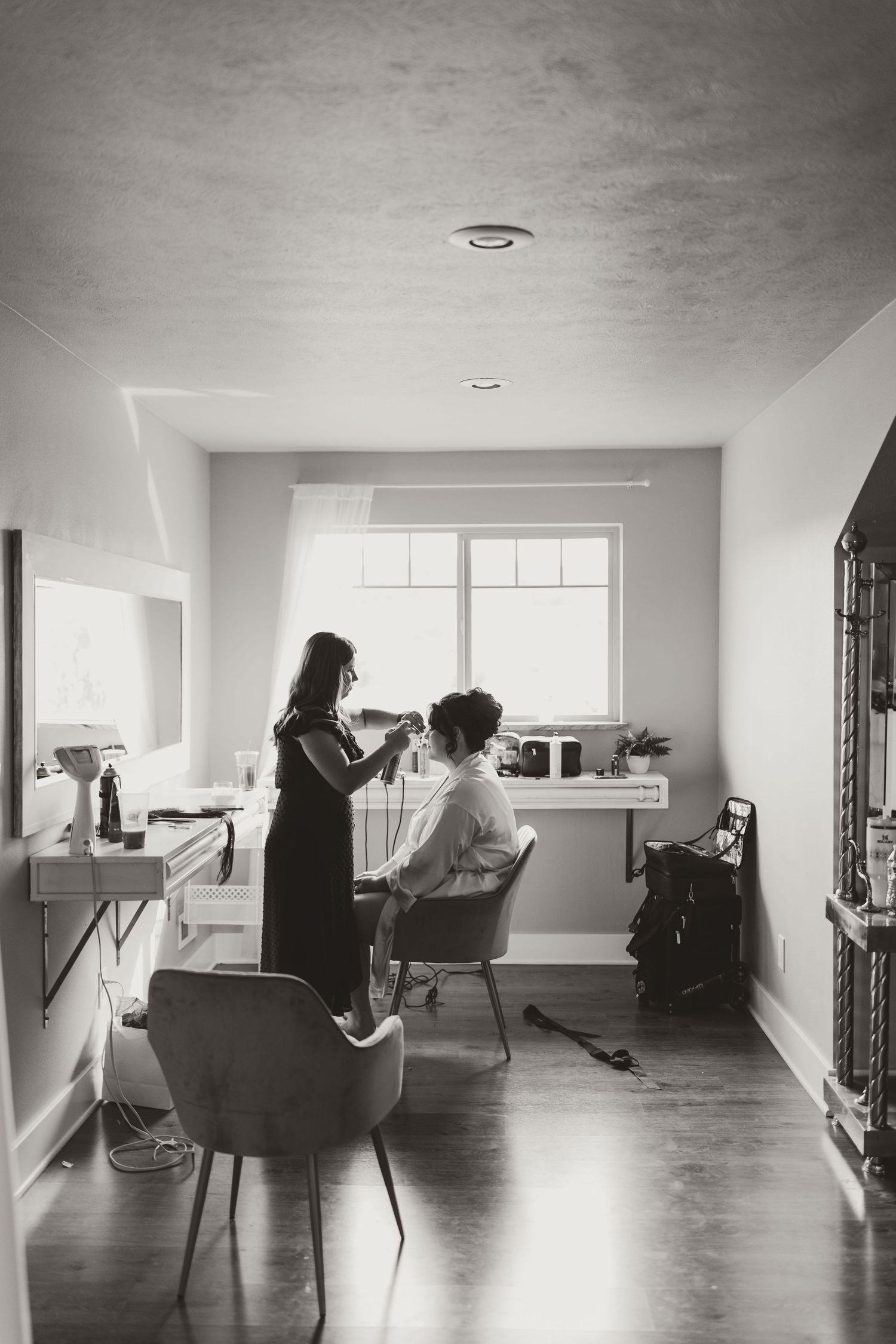Black and white photo of wedding day hair styling preparations in a bright room.