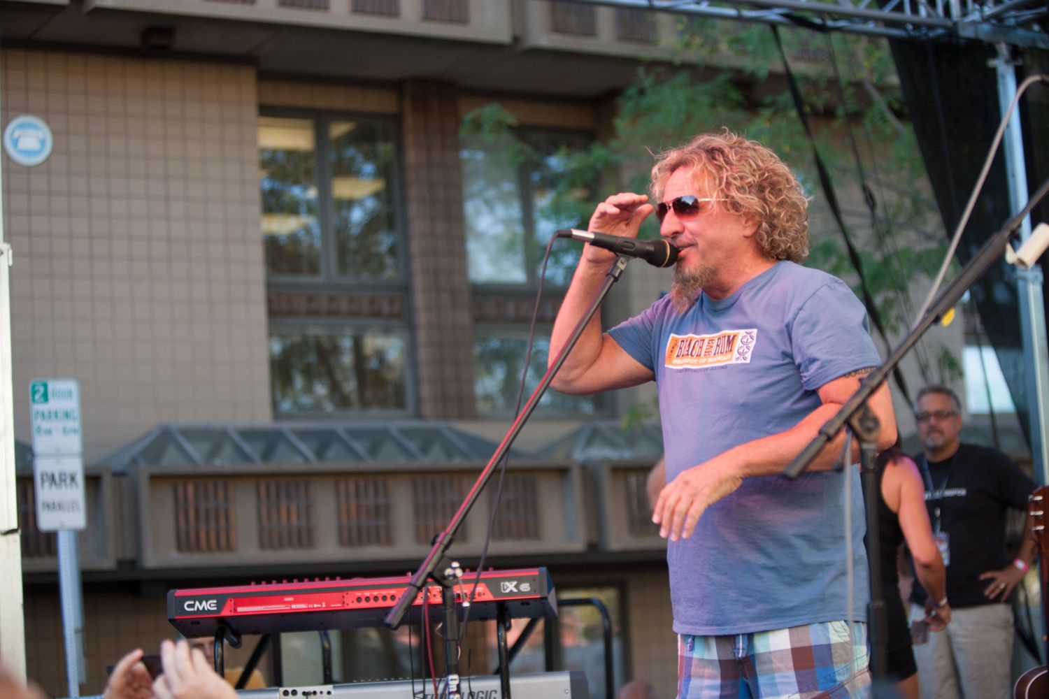 Musicians perform on stage at an outdoor concert with instruments and microphones set up.