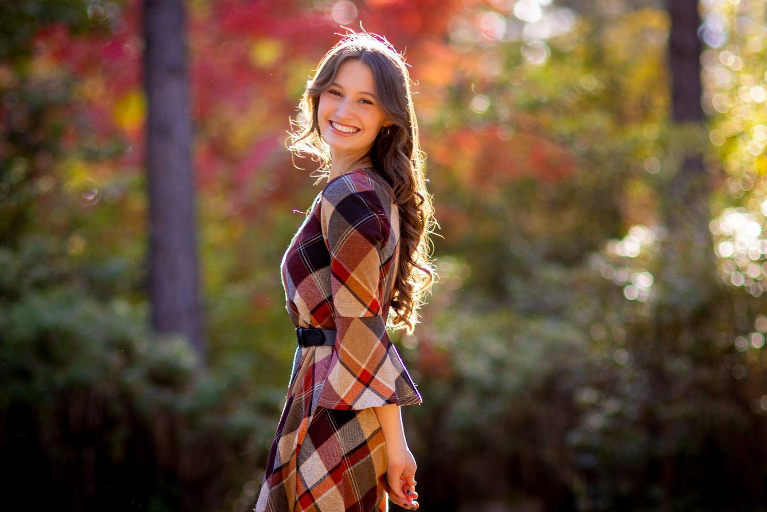 A plaid dress worn in an autumn forest setting with colorful fall foliage in the background.
