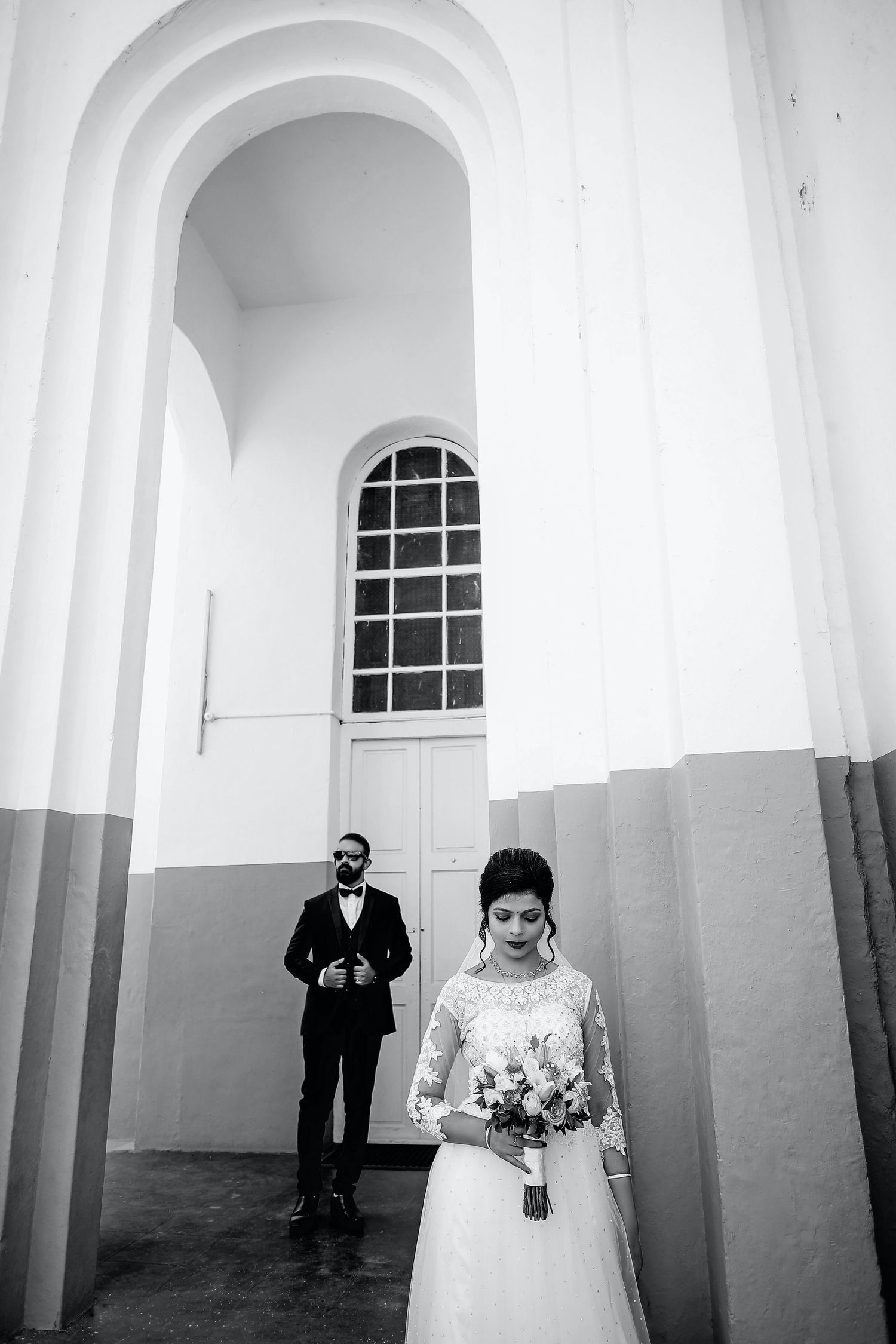 Bride looking at her bouquet and Groom looking somewhere outside of a building