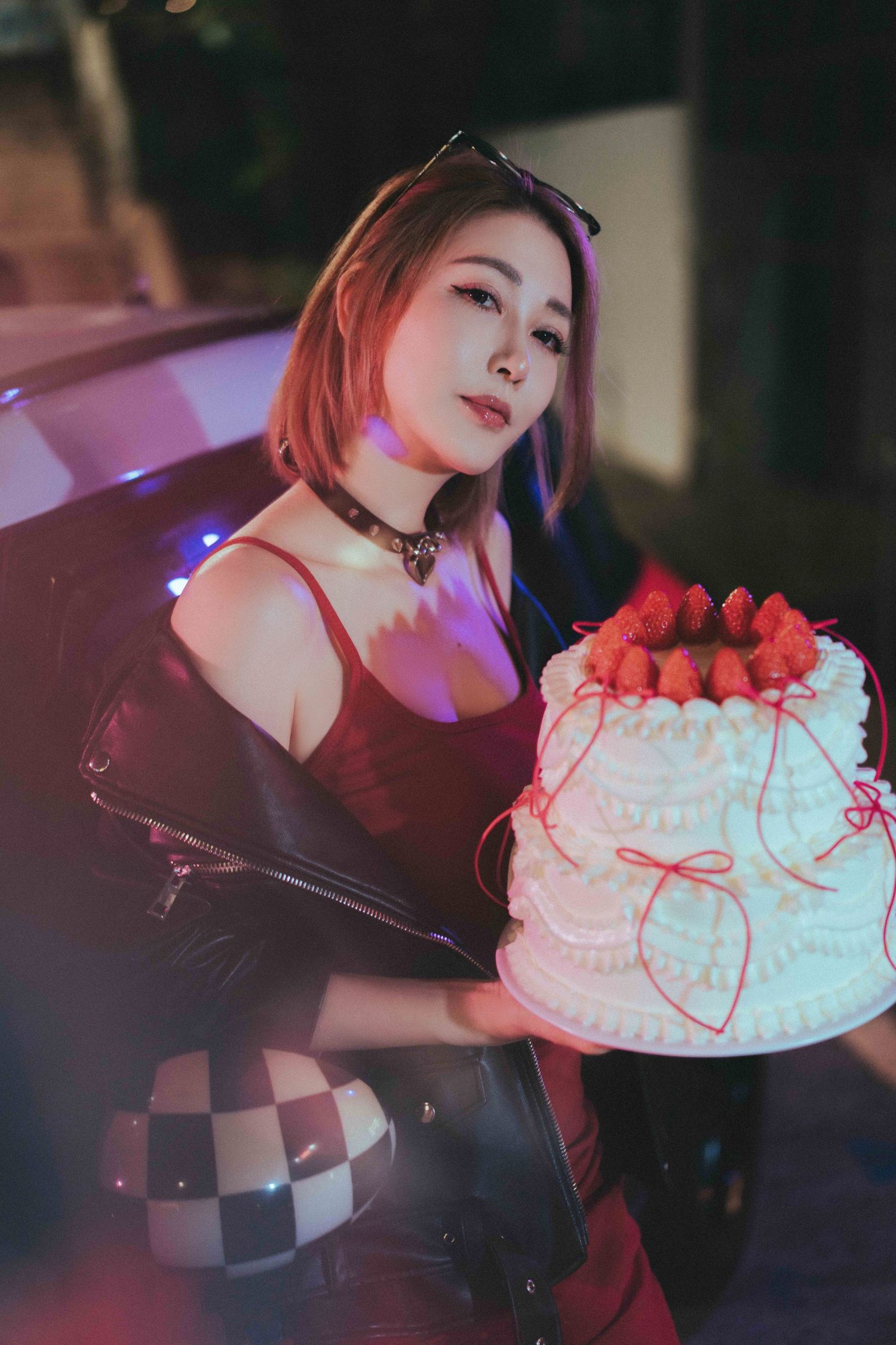 A series of moody photos showing someone in dark clothing holding a white decorated cake in dramatic lighting.一組氛圍感十足的照片，照片中一位身穿深色衣服的人