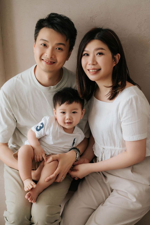 Happy Asian family portrait with parents and baby in matching white outfits smiling together.